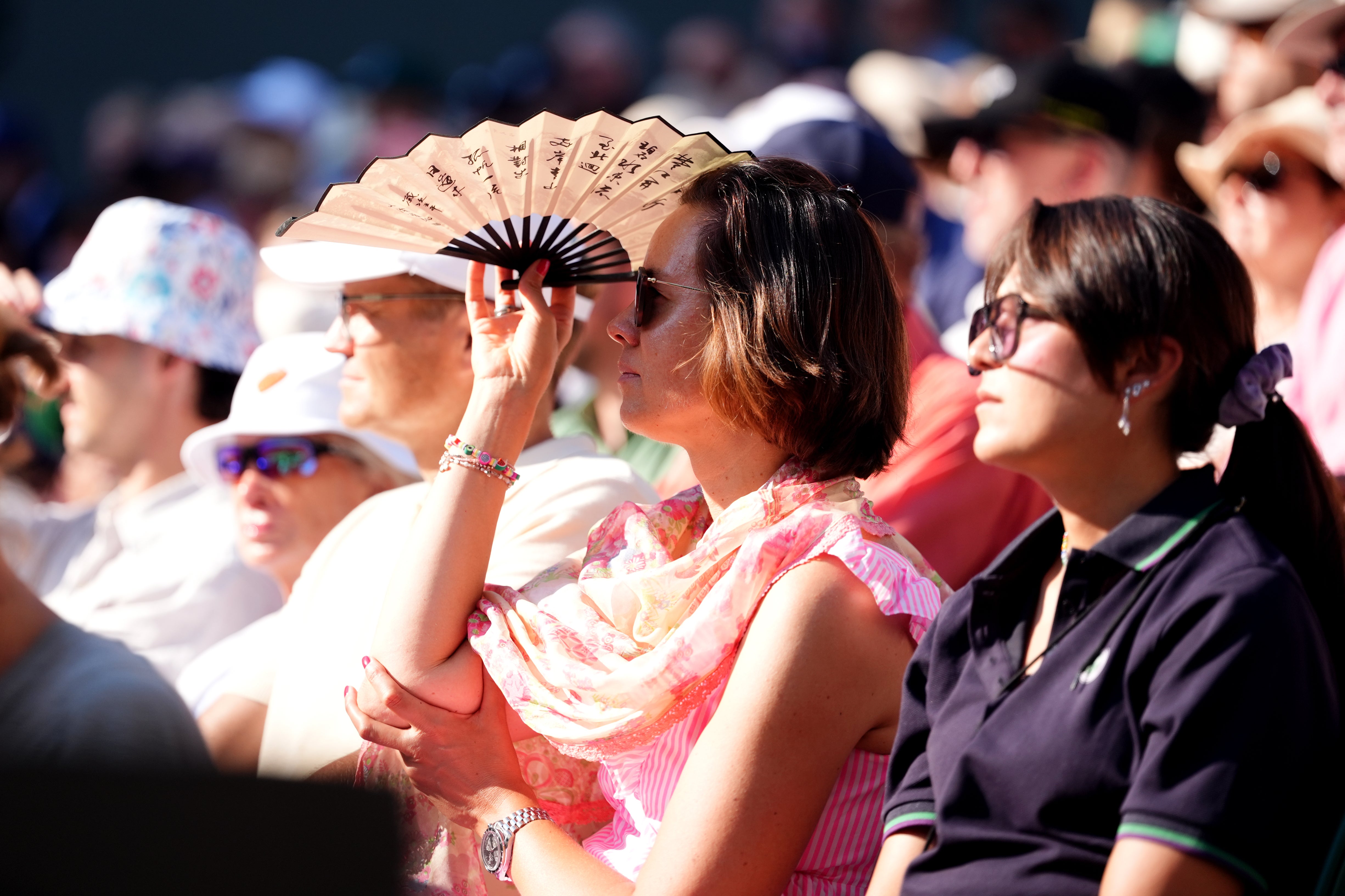 A spectator uses a fan to shield the sun from her eyes (Adam Davy/PA)