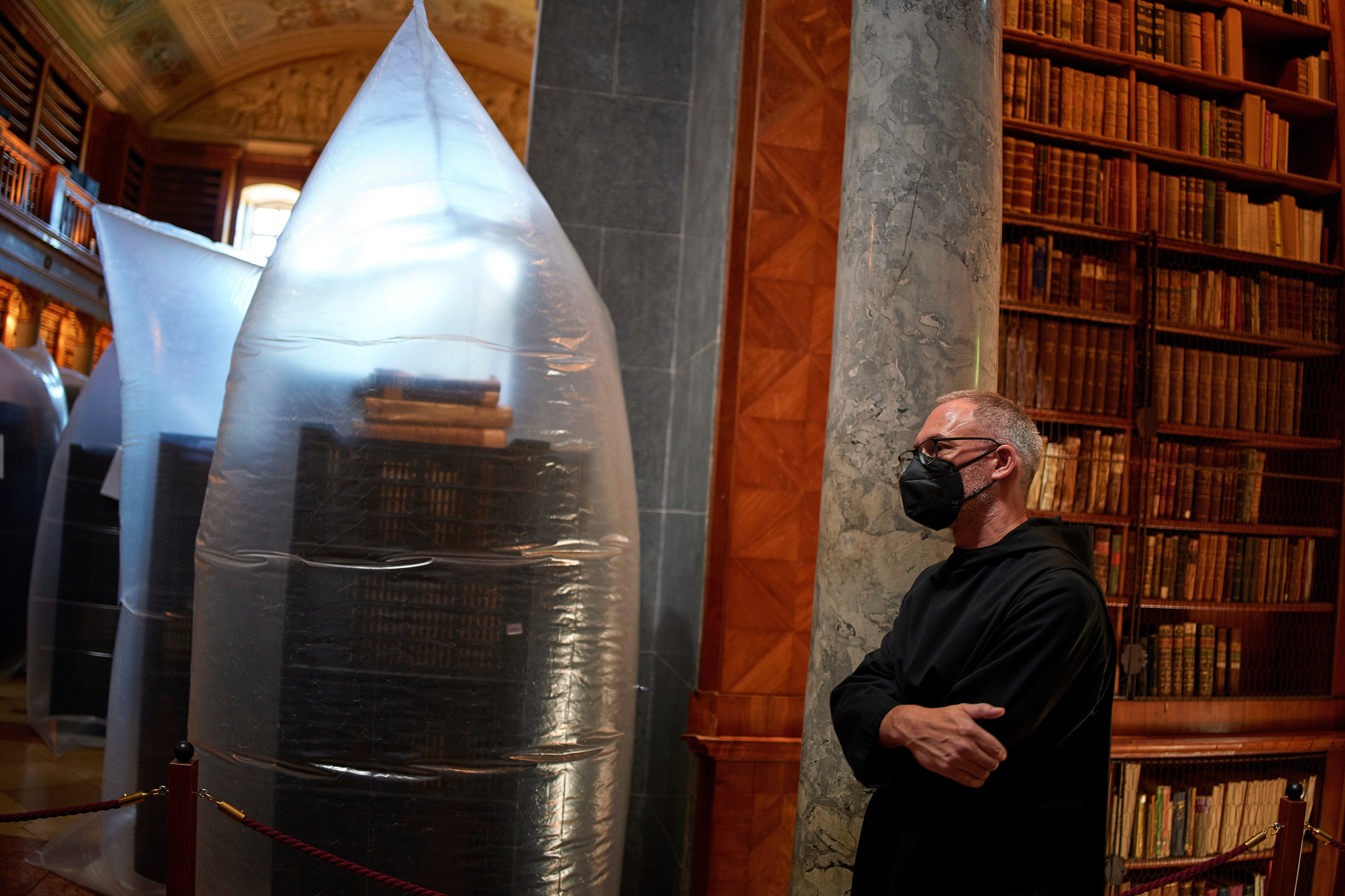 A priest wearing a face mask stands by as the books are hermetically sealed