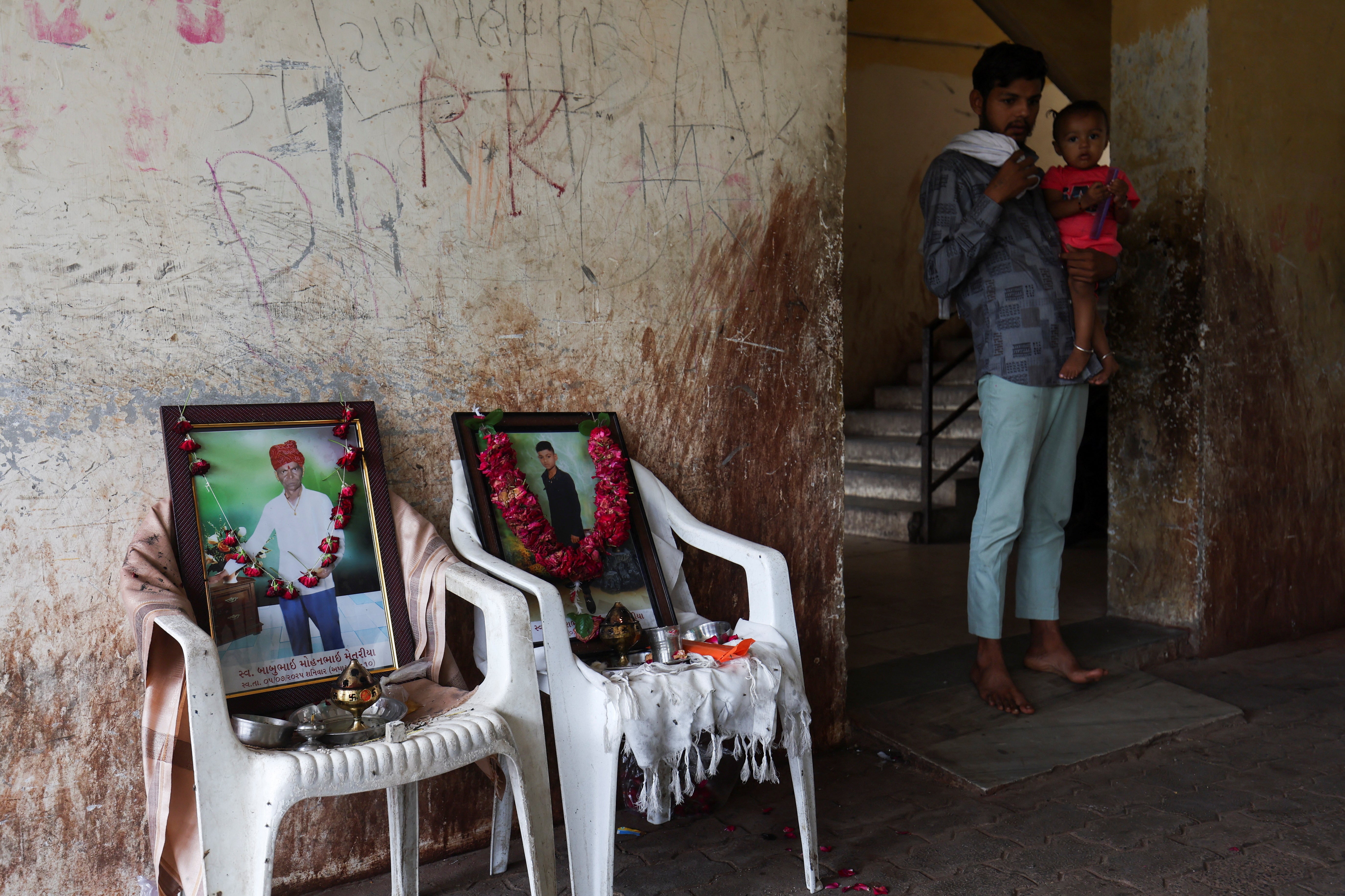 A family member with a child stands next to a photo of Akash Patni, who died after an Air India Boeing Dreamliner plane crashed during takeoff from the Ahmedabad airport