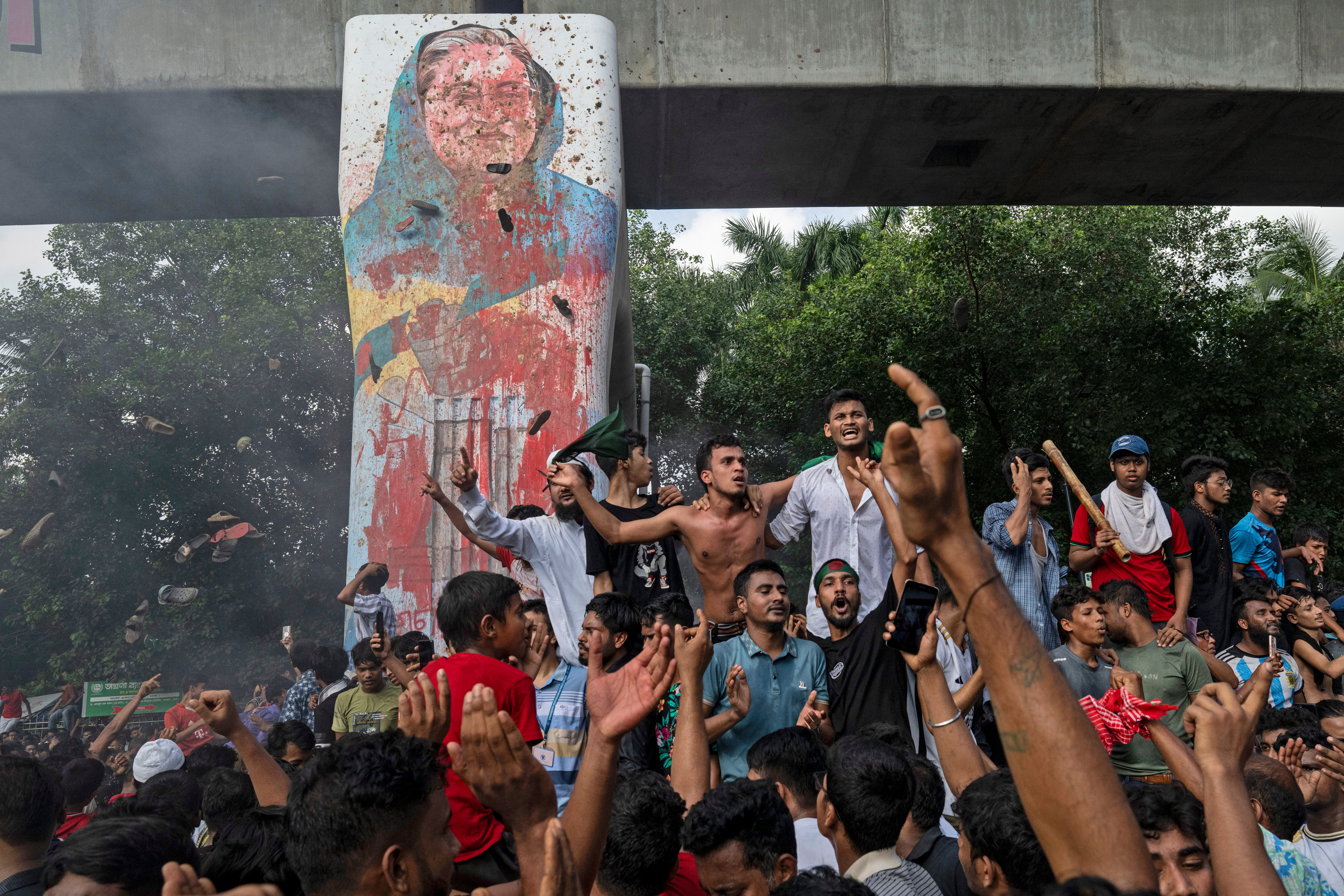 Protesters celebrate beside a defaced portrait of Hasina after her fall from power in Dhaka