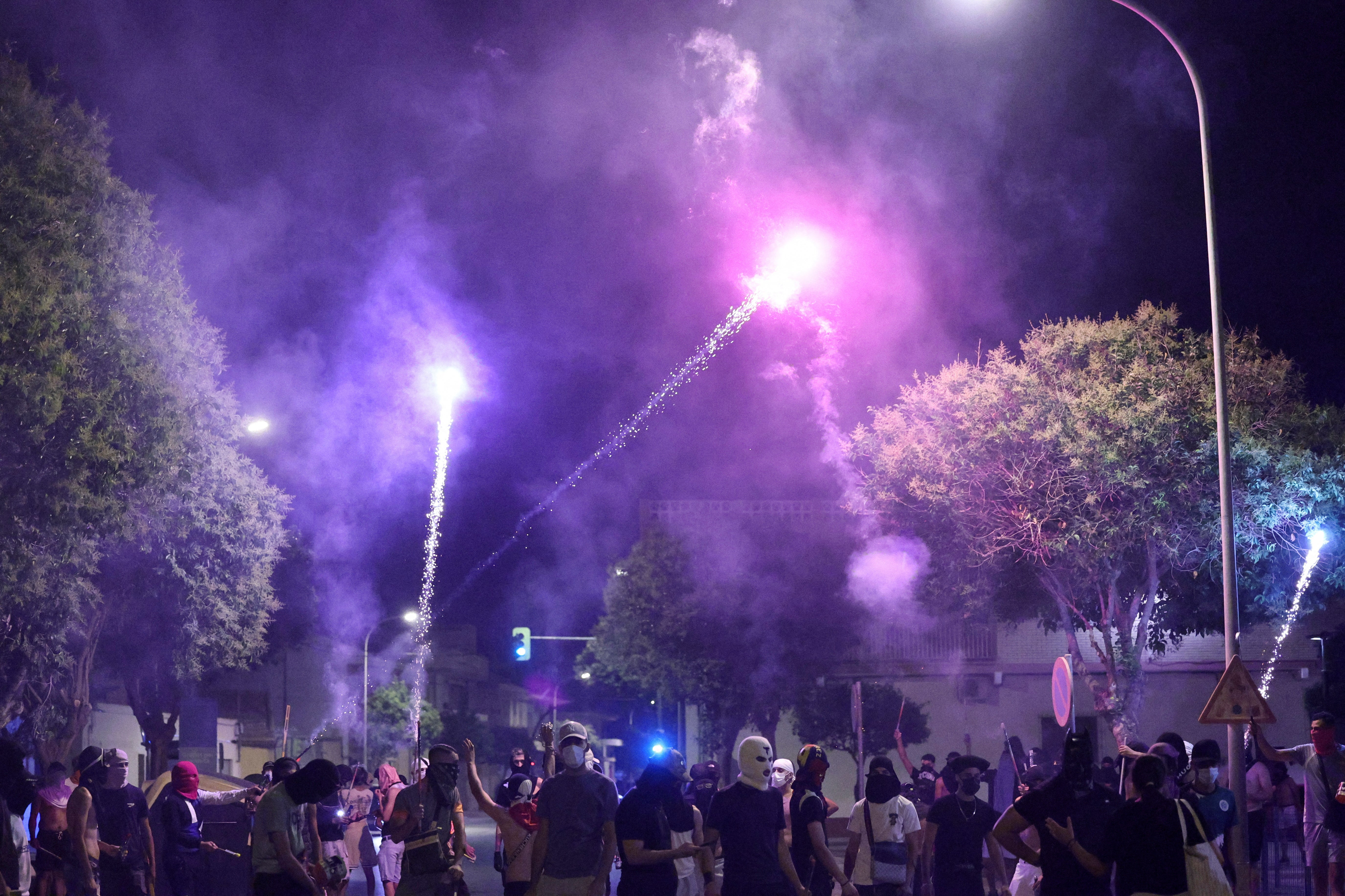 People gather on a street as fireworks streak through the night sky