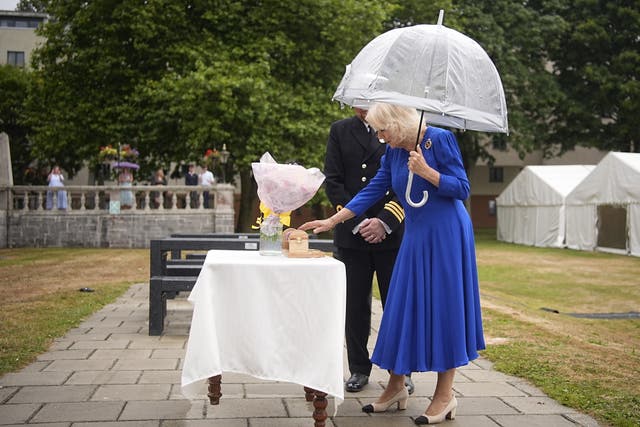 <p>Queen Camilla is presented with flowers and a cling film roll holder during a garden party for the HMS Astute Ship's Company and their families at HMS Drake</p>