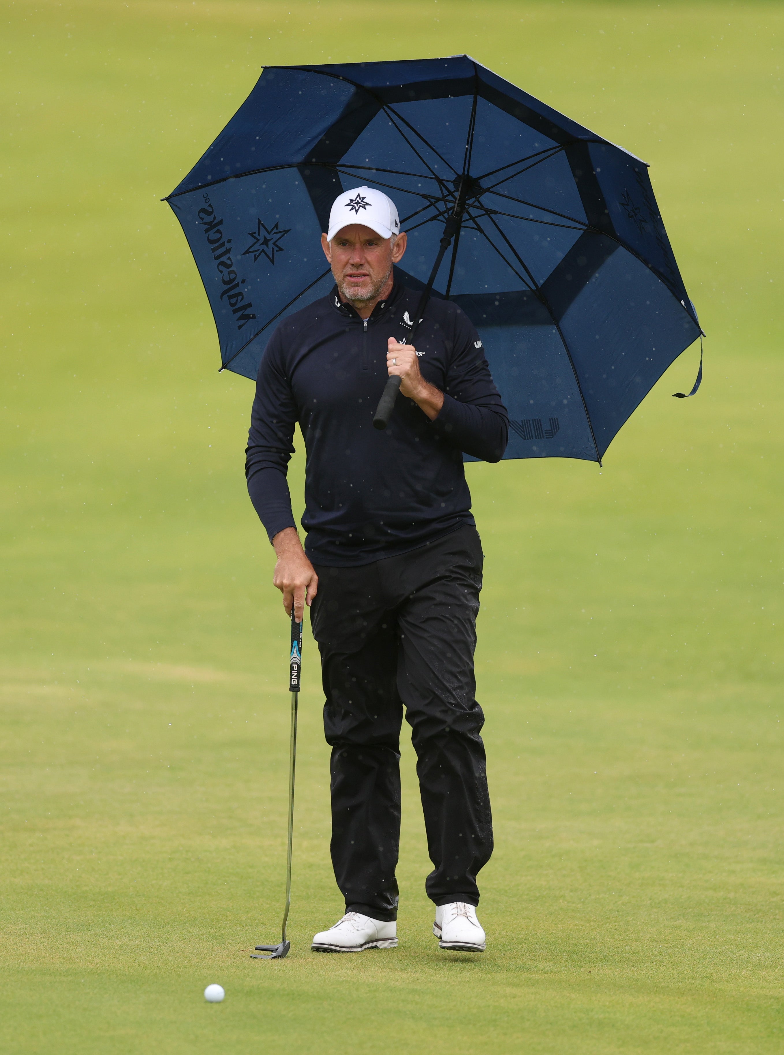 Lee Westwood of England stands with an umbrella