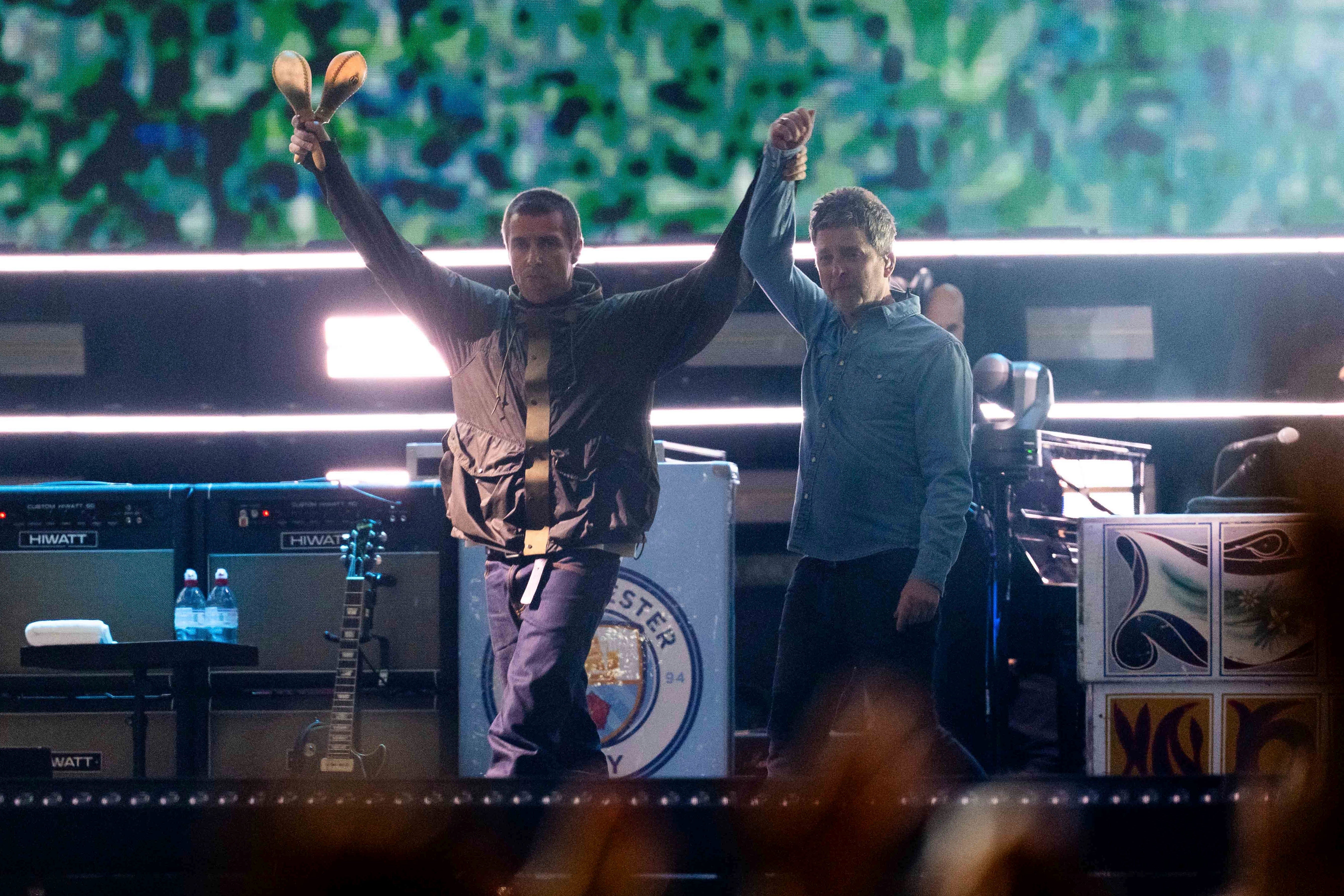 Noel and Liam hold their hands aloft as they arrive onstage in Cardiff for the first Oasis reunion gig