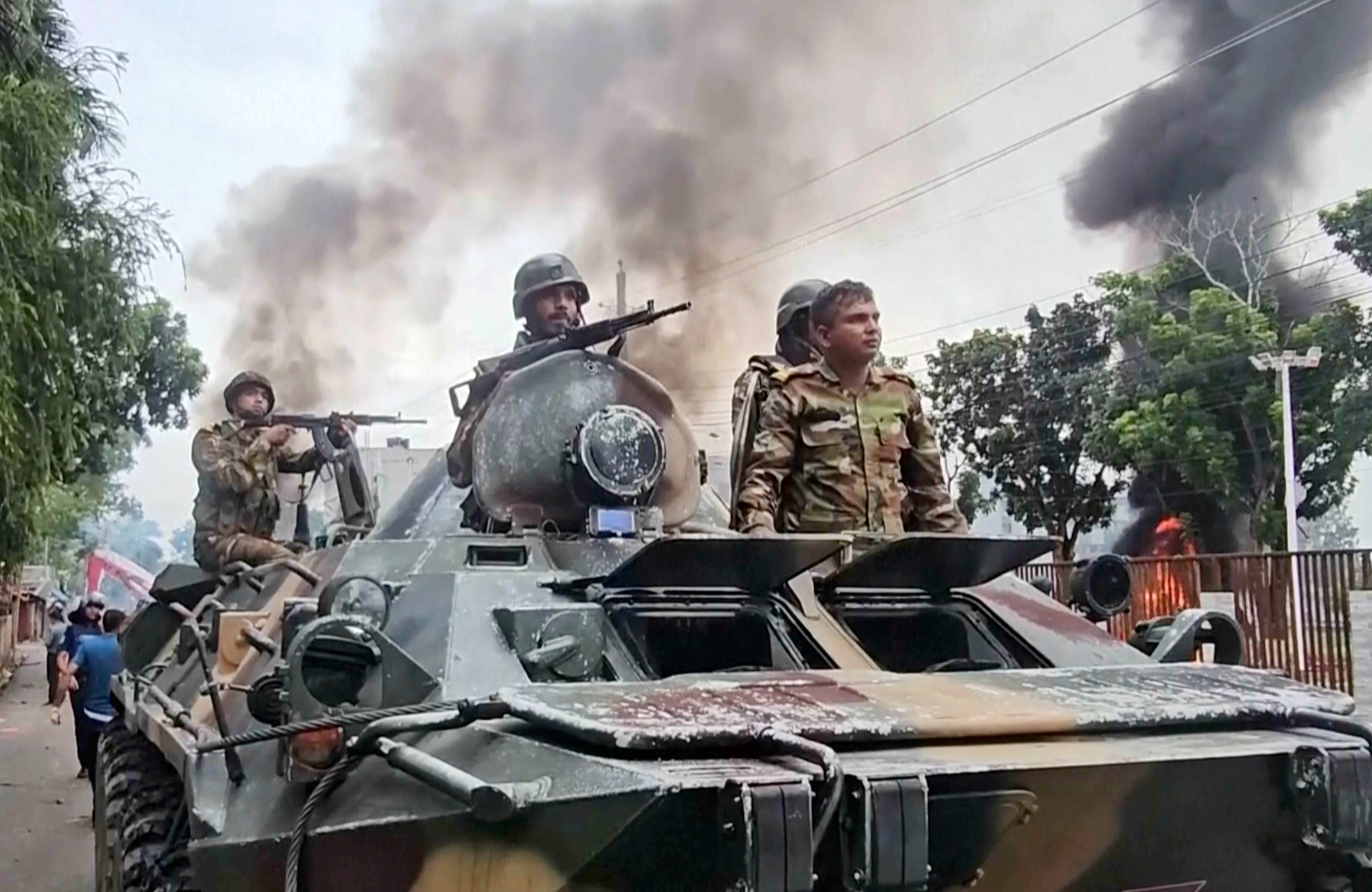 Smoke rises behind an armored vehicle as supporters of the ousted Prime Minister Sheikh Hasina clash