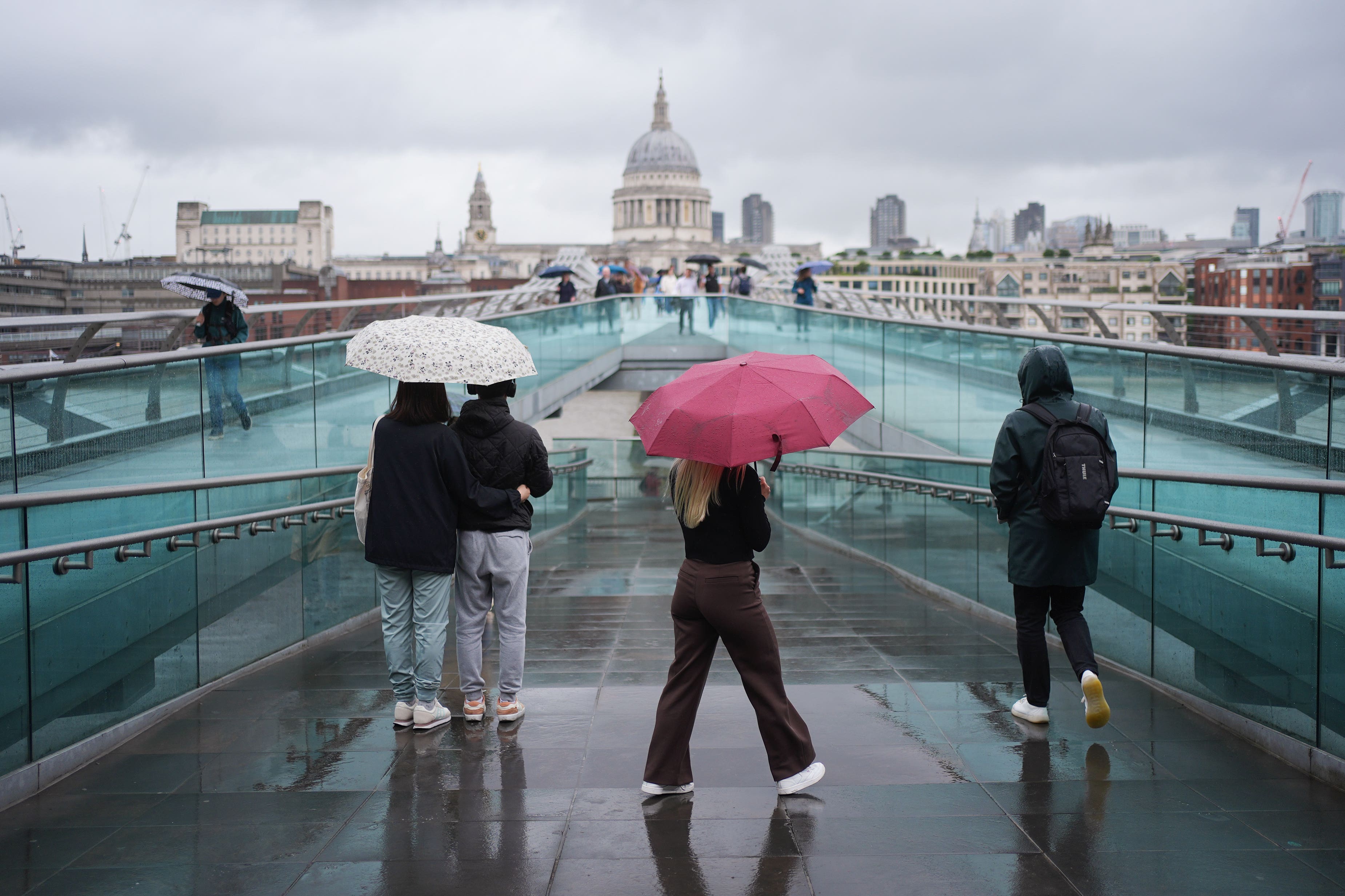 People with umbrellas walking along the Millennium Bridge (PA)