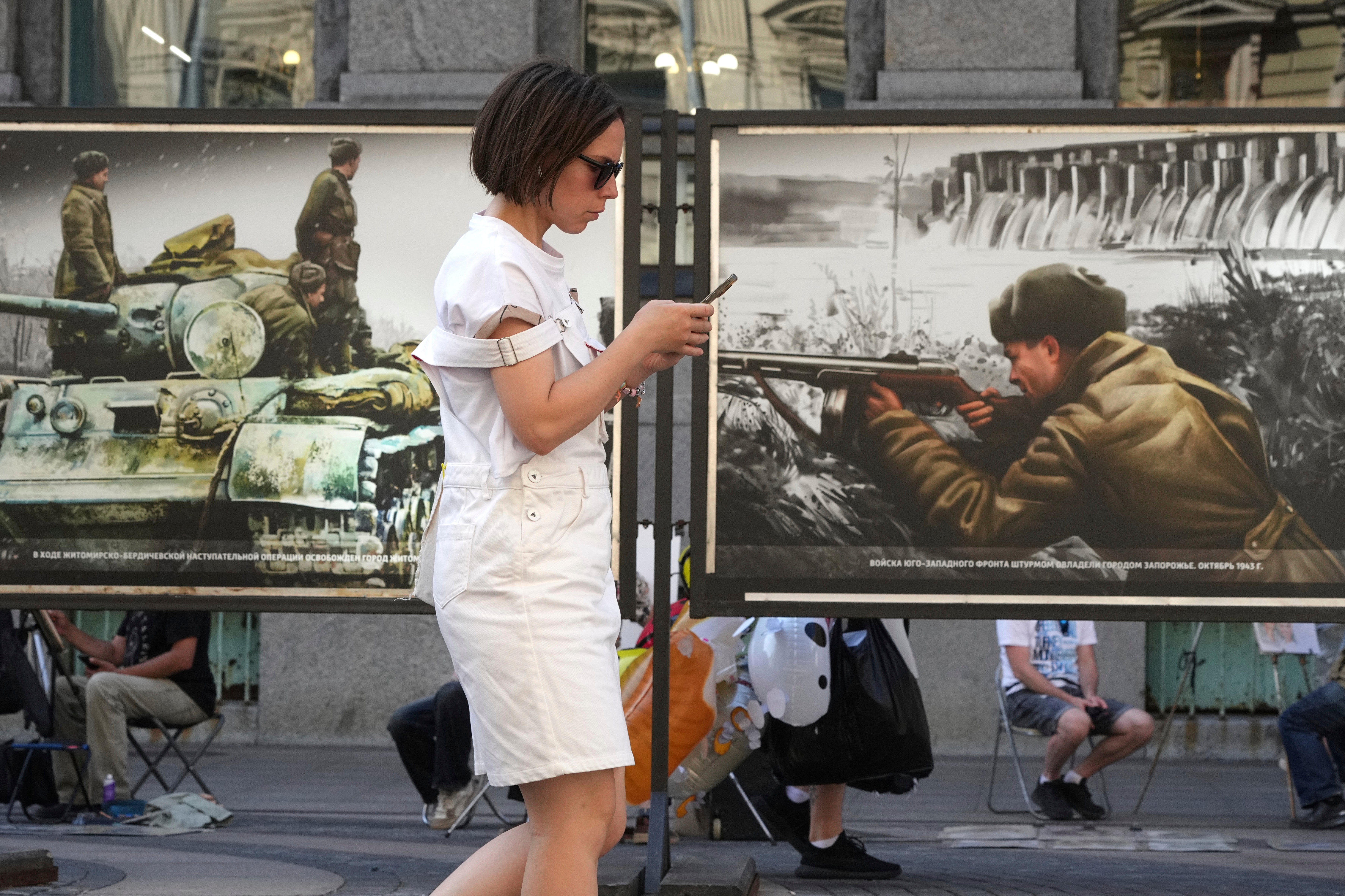 A woman looks at her phone while passing by a series of World War II-era colourised images