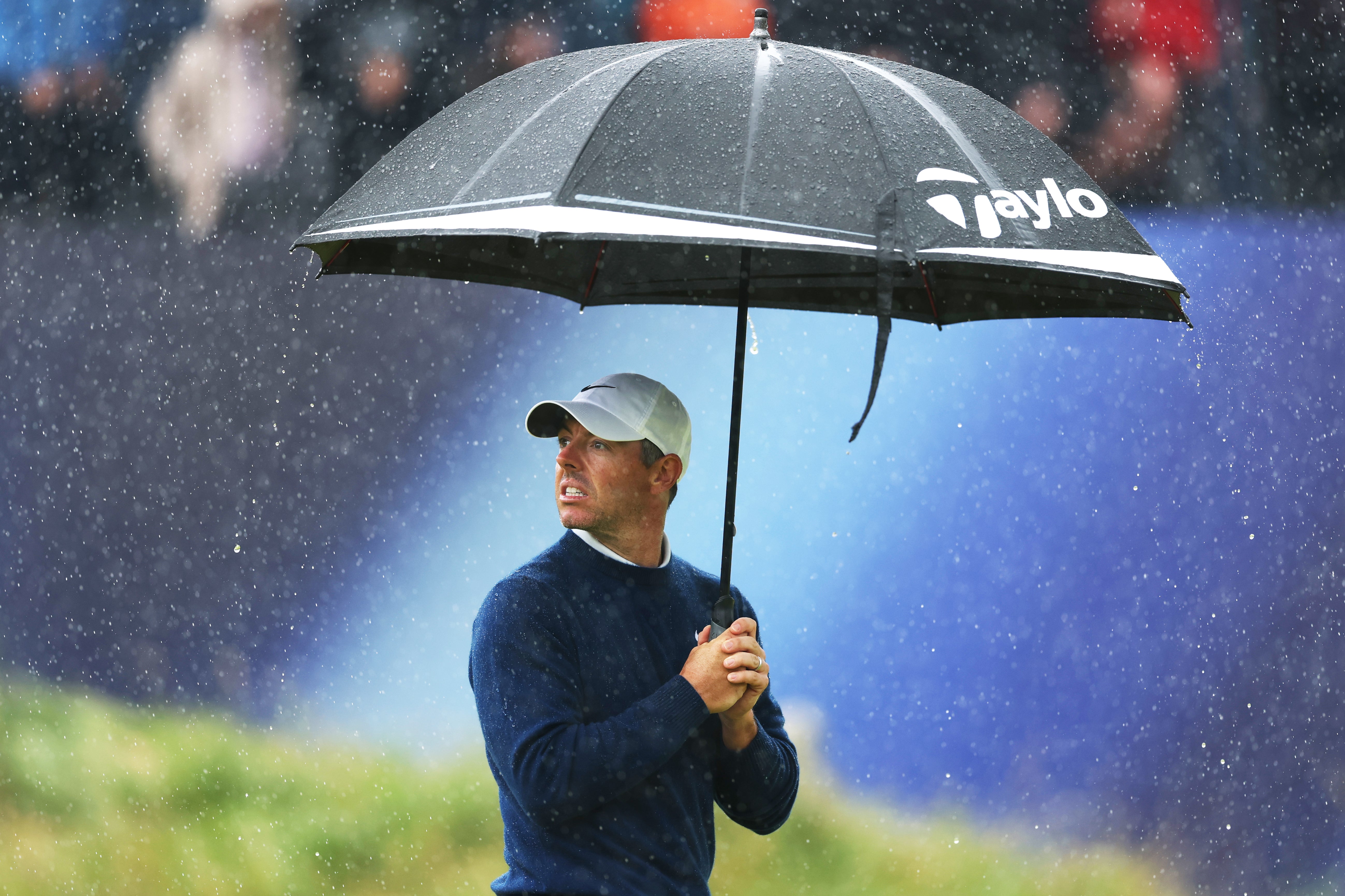 Rory McIlroy of Northern Ireland holds an umbrella in the rain on the 18th hole