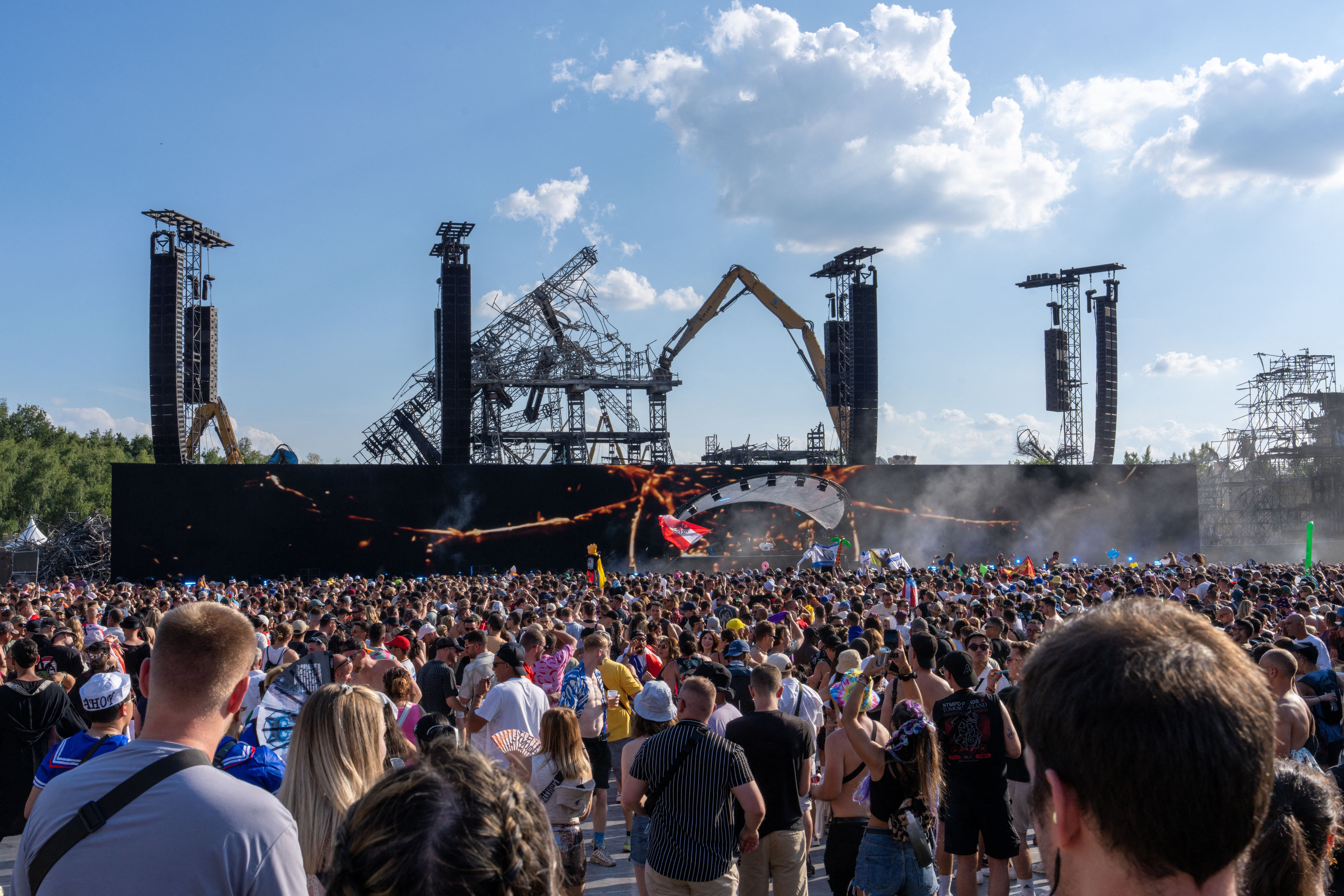 Festival-goers gather before the burnt main stage during its dismantling on Friday