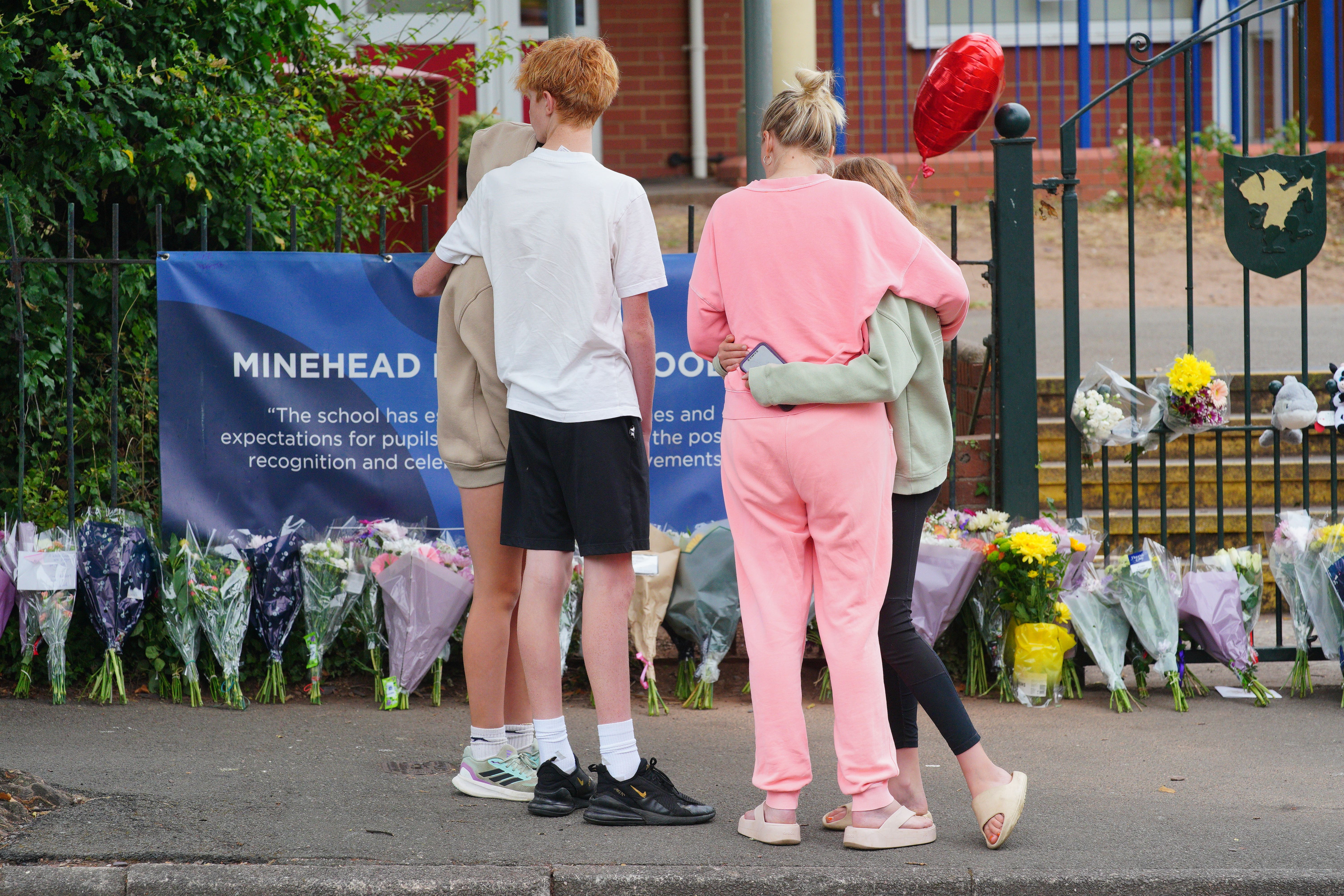 People comfort each other as they look at the floral tributes at the entrance to the Minehead Middle School (Ben Birchall/PA)