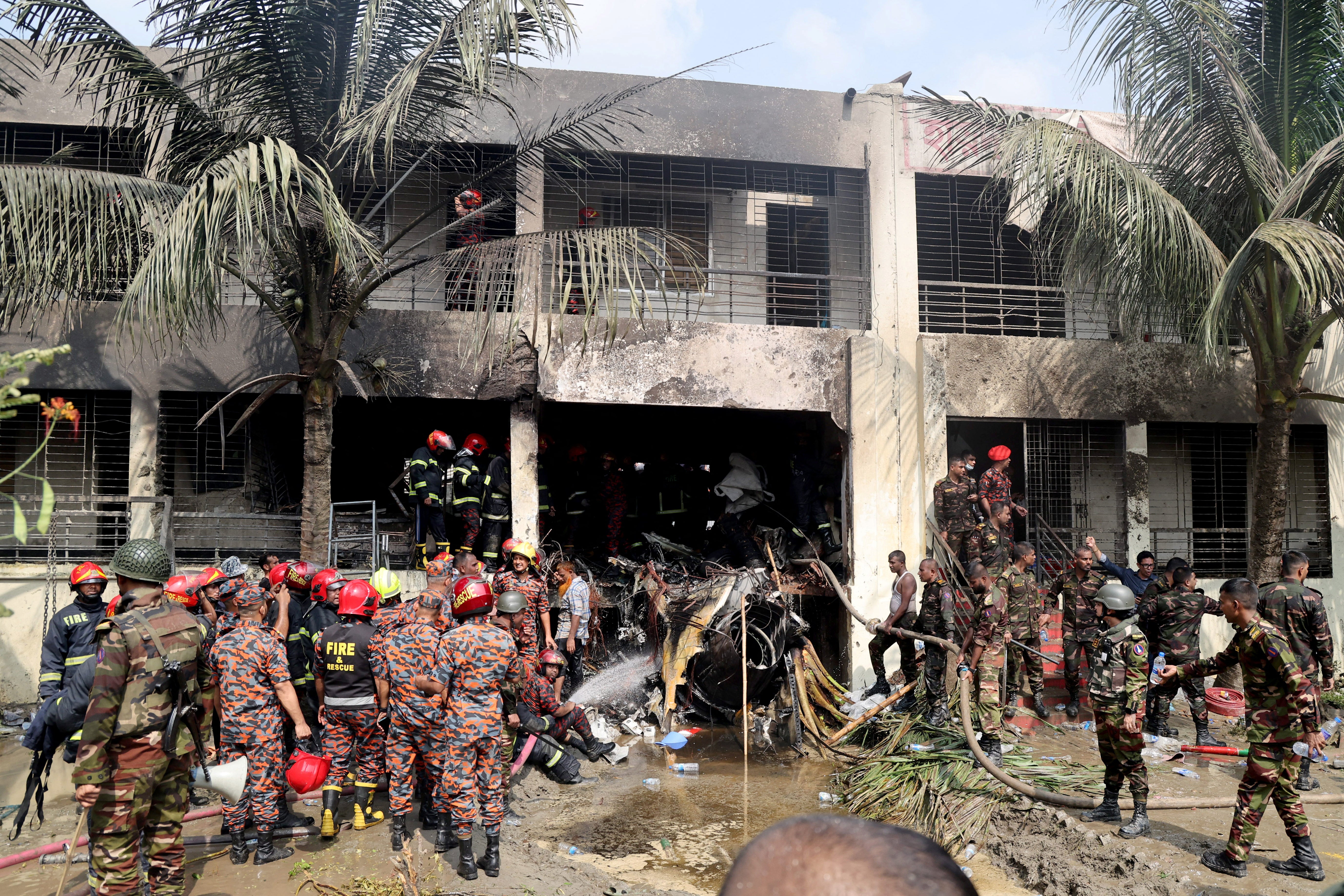 <p>Firefighters and soldiers work next to the wreckage of an military training aircraft after it crashed in Dhaka, Bangladesh, on 21 July 2025</p>