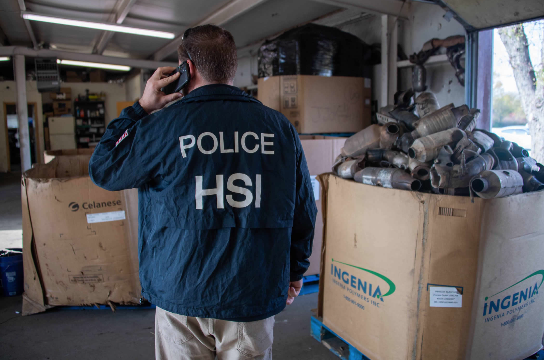 A member of U.S. Department of Homeland Security Investigations next to a box filled with stolen catalytic converters