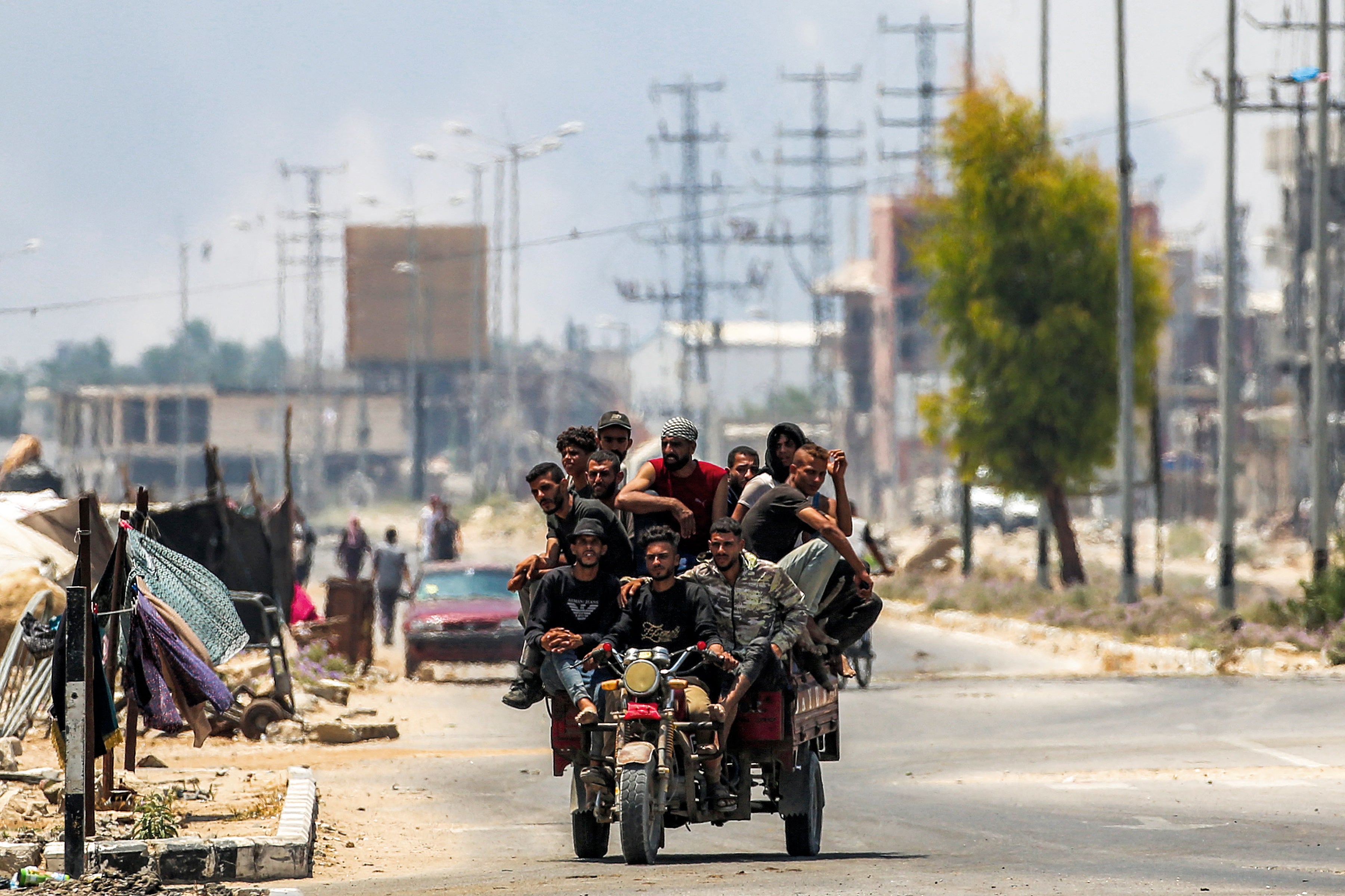 Men ride in a tricycle cart in Deir al-Balah in central Gaza while smoke billows from Israeli bombardment on 21 July 2025