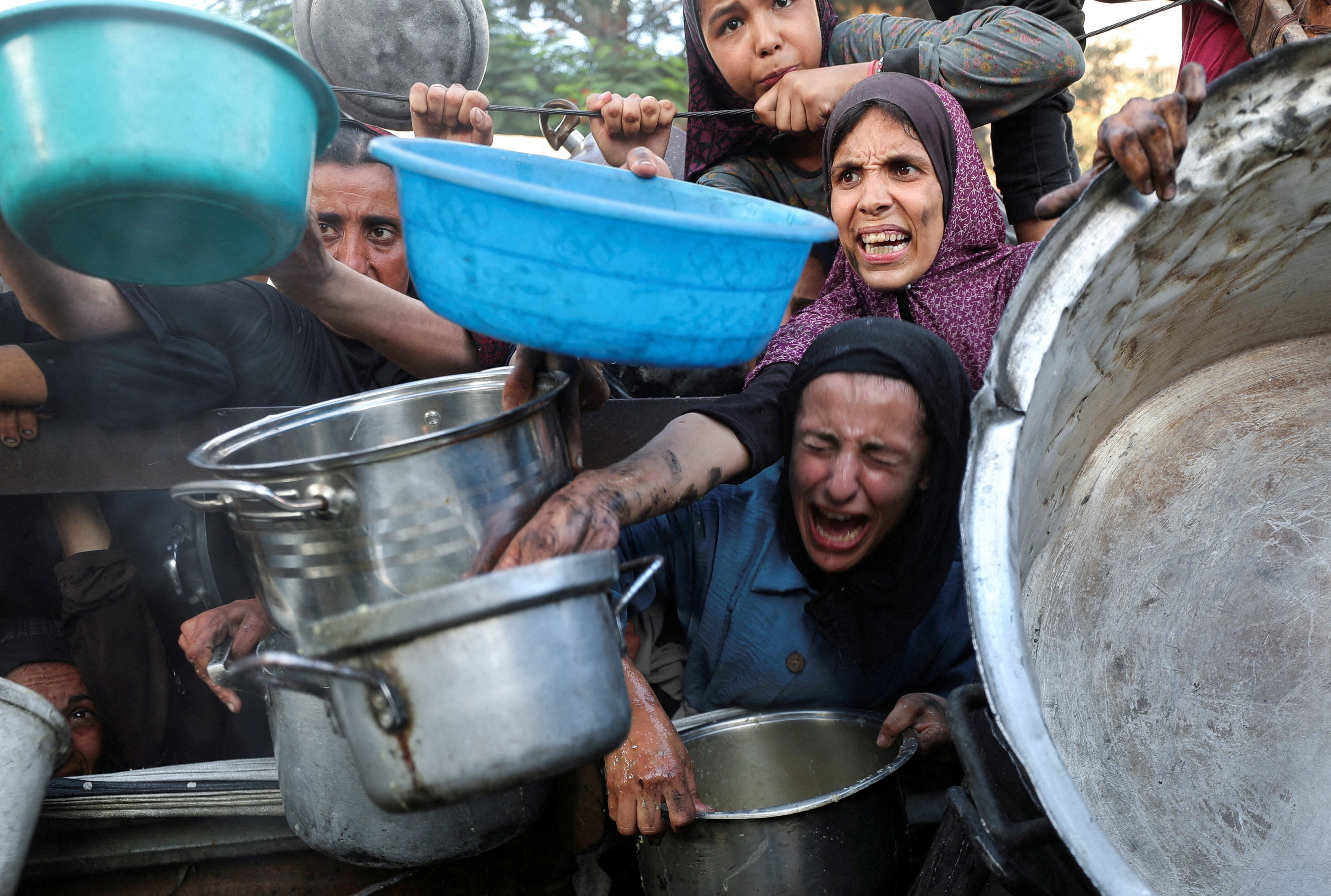 Palestinians react as they ask for food from a charity kitchen, amid a hunger crisis, in Gaza City