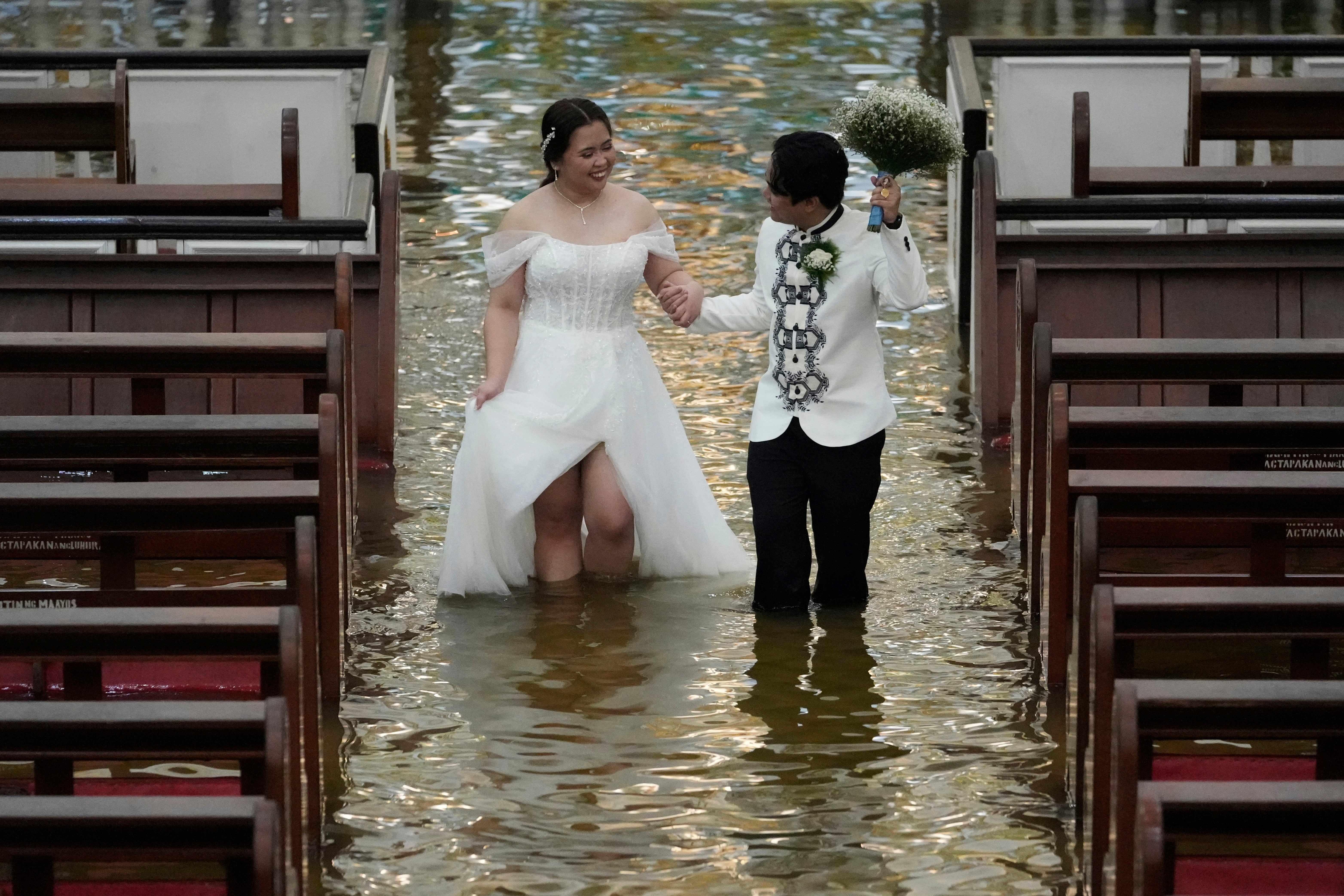 Newlyweds Jade Rick Verdillo (right) and Jamaica Aguilar walk hand in hand during their wedding at the flooded Barasoain church in Malolos, Bulacan province, Philippines on Tuesday, 22 July 2025