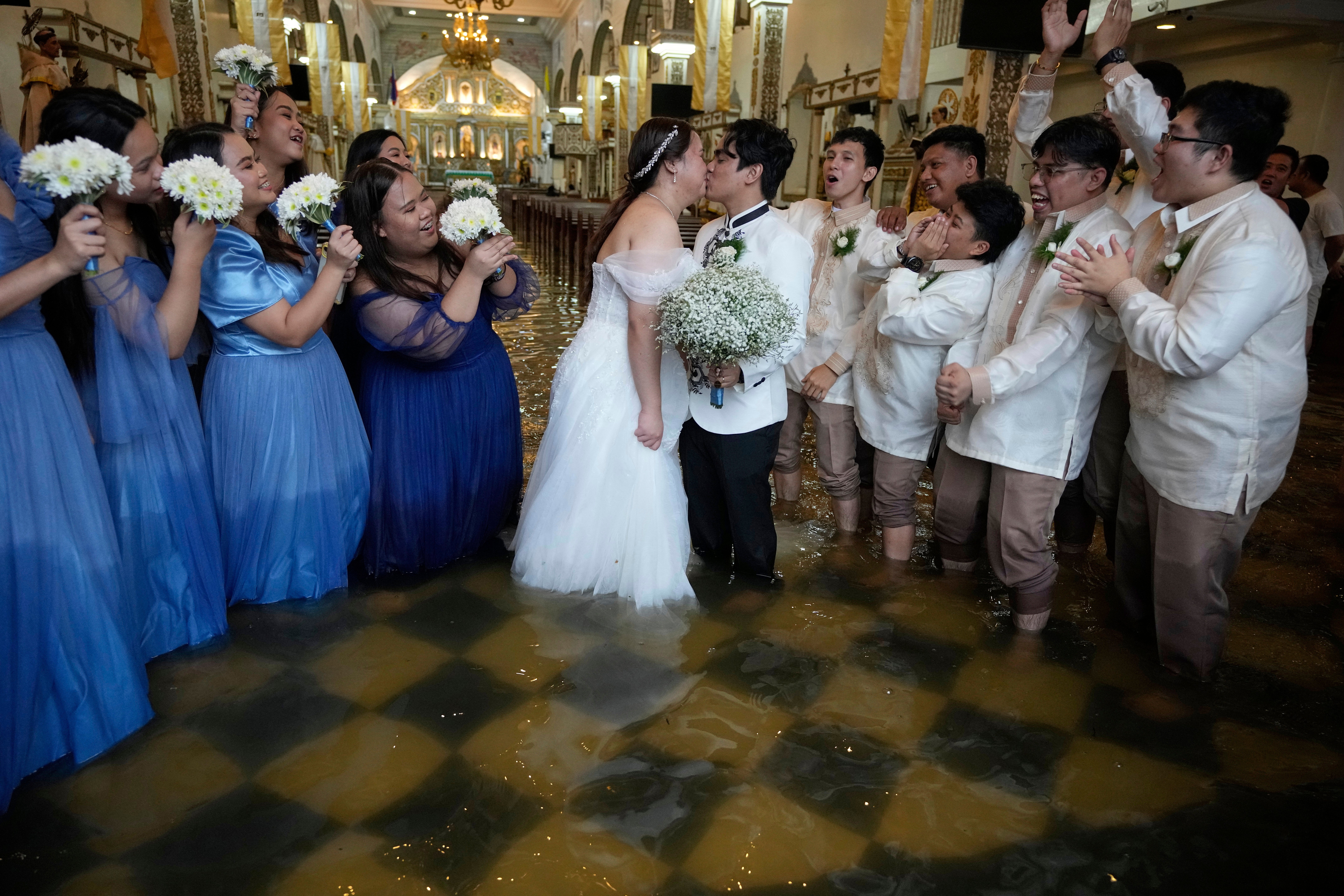 Newlyweds Jade Rick Verdillo, centre, and Jamaica Aguilar pose with a kiss as guests cheer at the flooded Barasoain church in Malolos, Bulacan province, Philippines