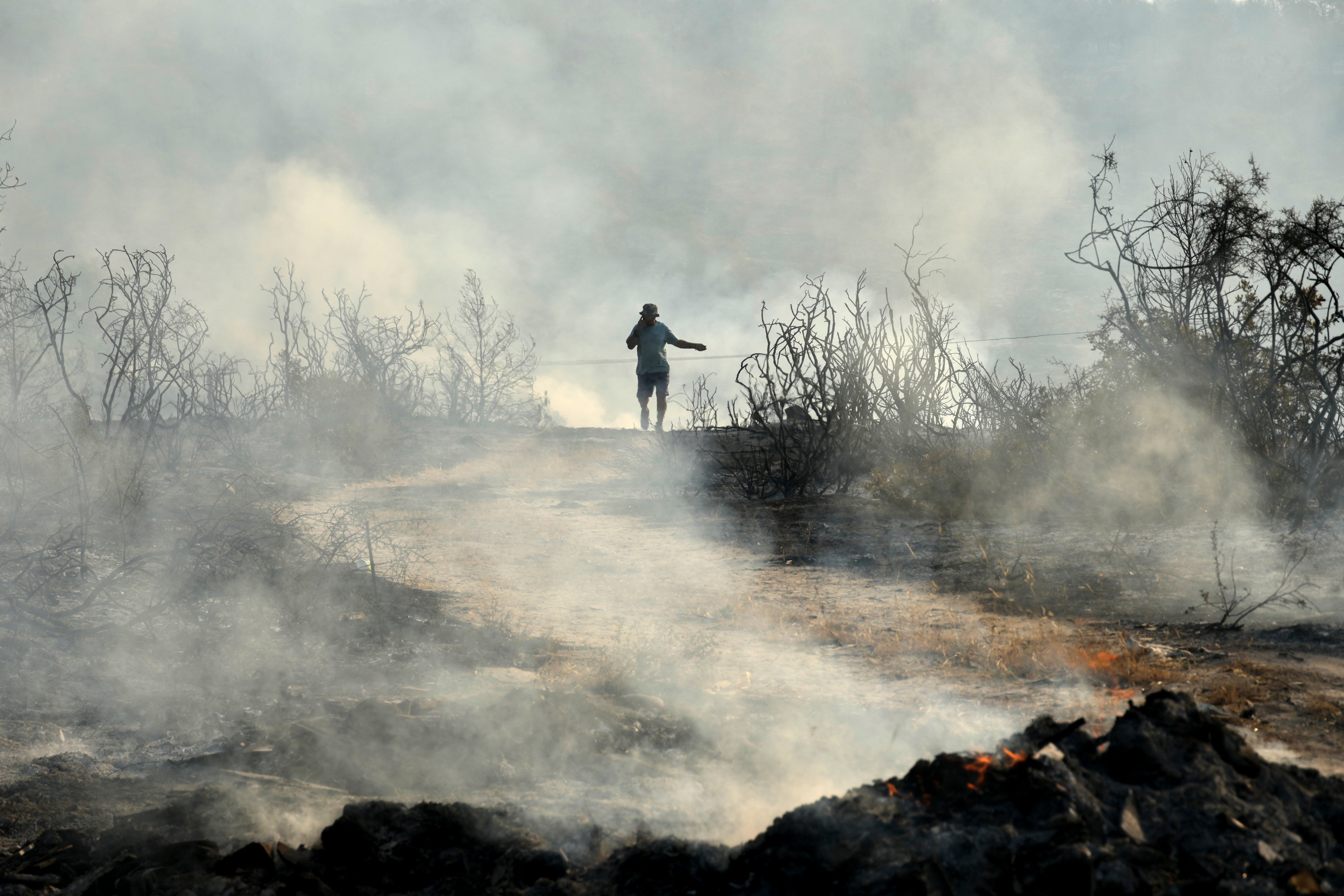 A man speaking on his cellphone walks through a burned area in Souni village