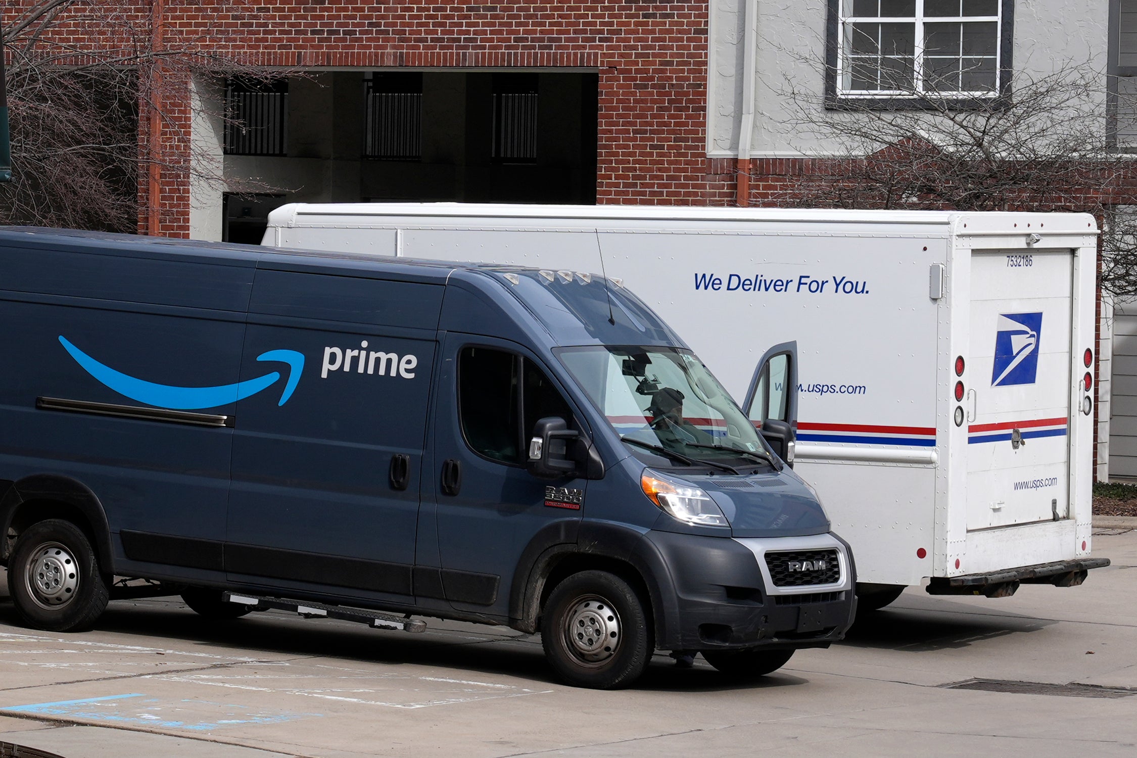 An Amazon Prime truck and a U.S. Postal Service truck make deliveries at an apartment complex in Pittsburgh
