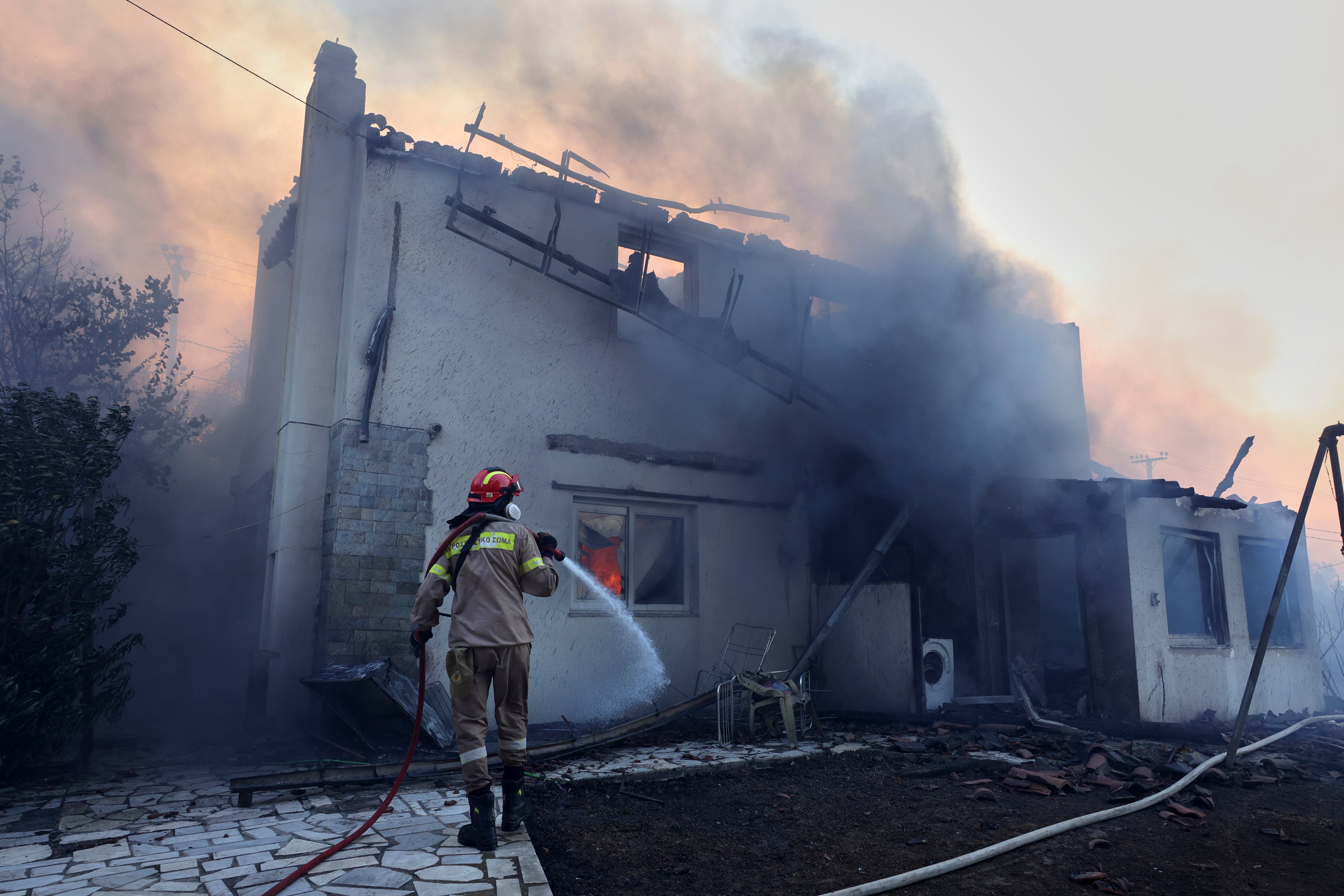 A firefighter tries to extinguish the blazes at a burning house during a wildfire, in the northwestern suburb of Kryoneri, in Athens, Greece, Saturday, July 26, 2025. (AP Photo/Yorgos Karahalis)