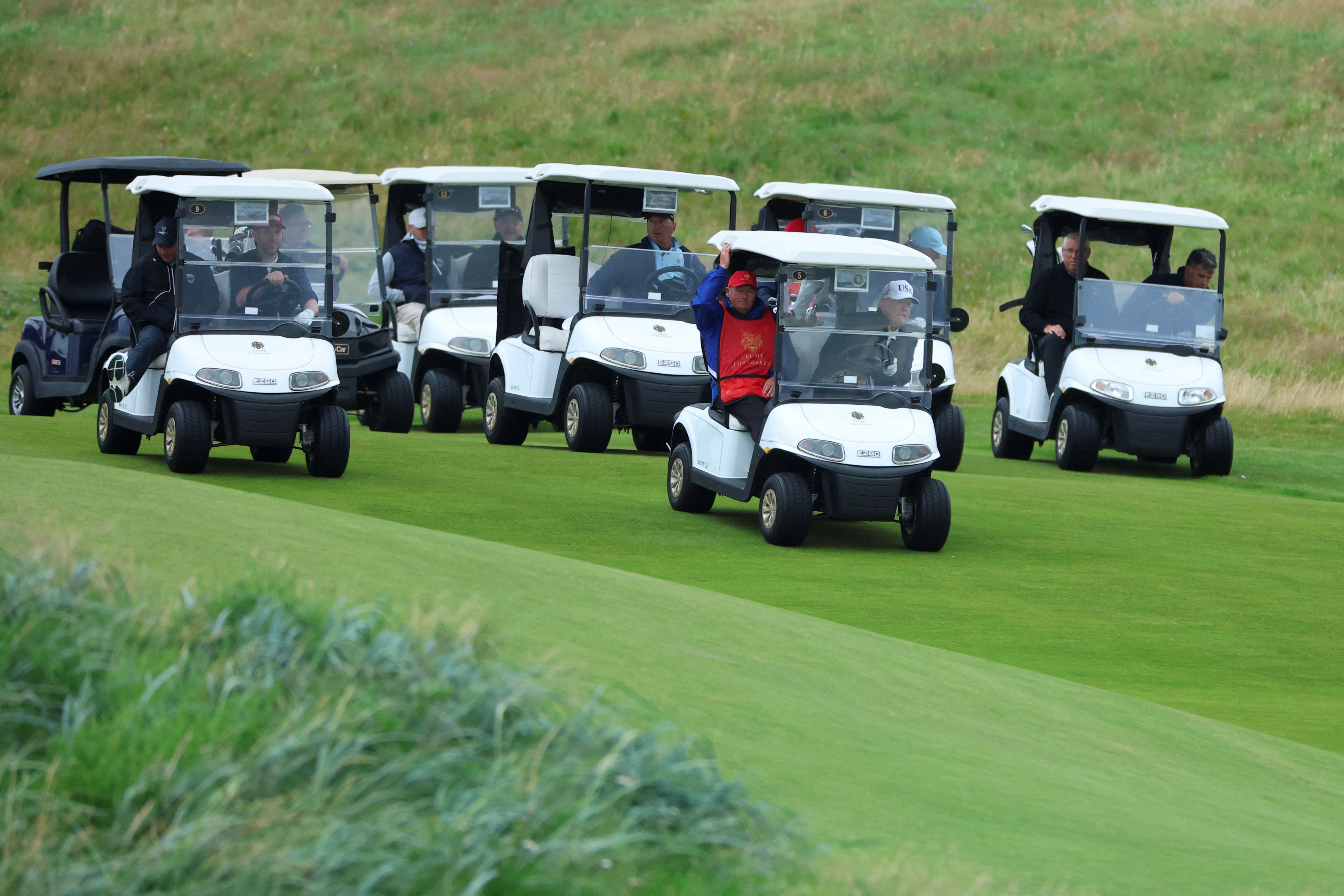 Wearing a white baseball cap branded USA, the US president waved to journalists as he arrived at his Turnberry golf resort in a white golf buggy