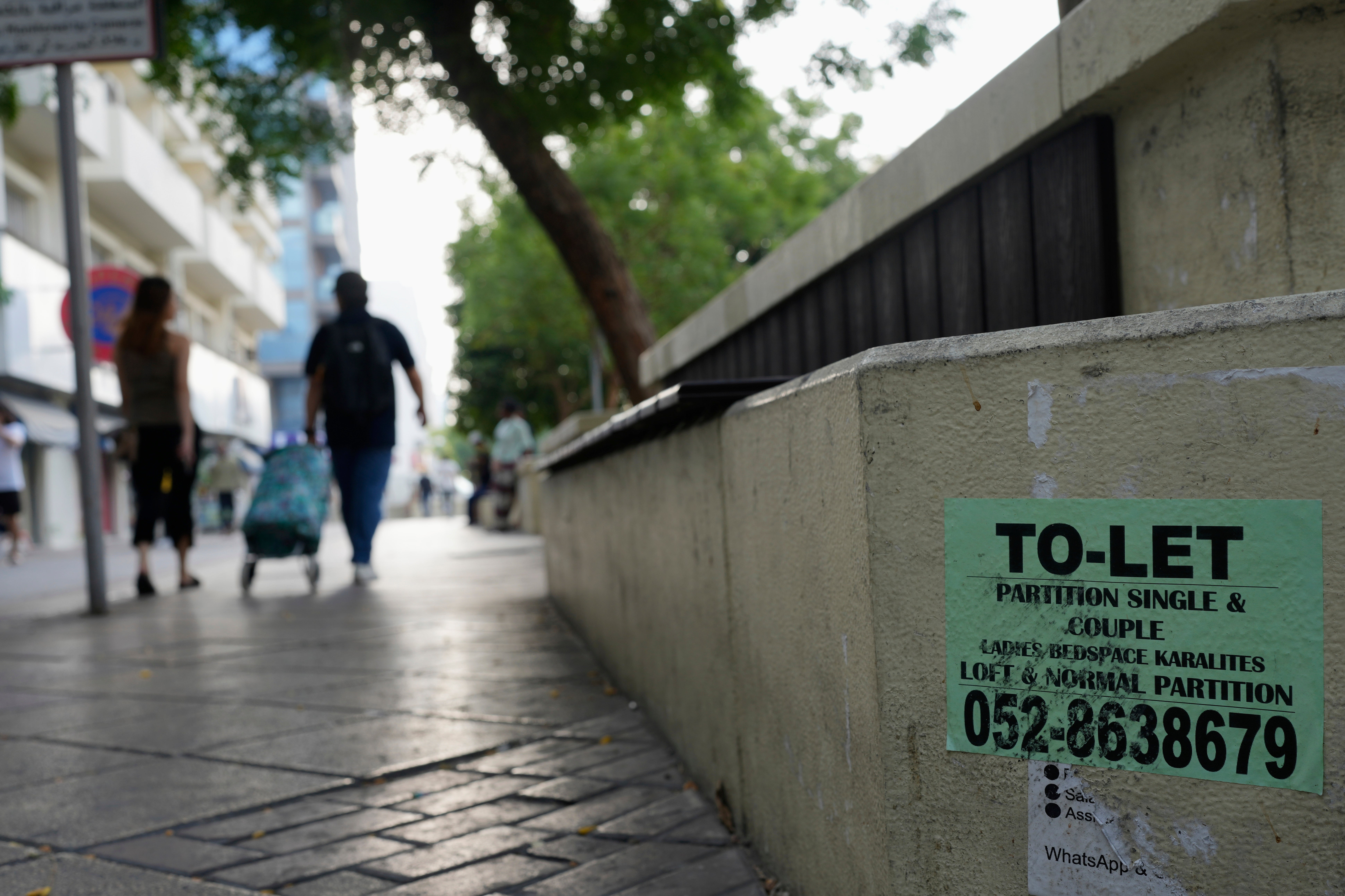 People walk past a concrete bench plastered with advertisements for inexpensive, partitioned housing in Dubai, United Arab Emirates, Friday, July 4, 2025. (AP Photo/Altaf Qadri)