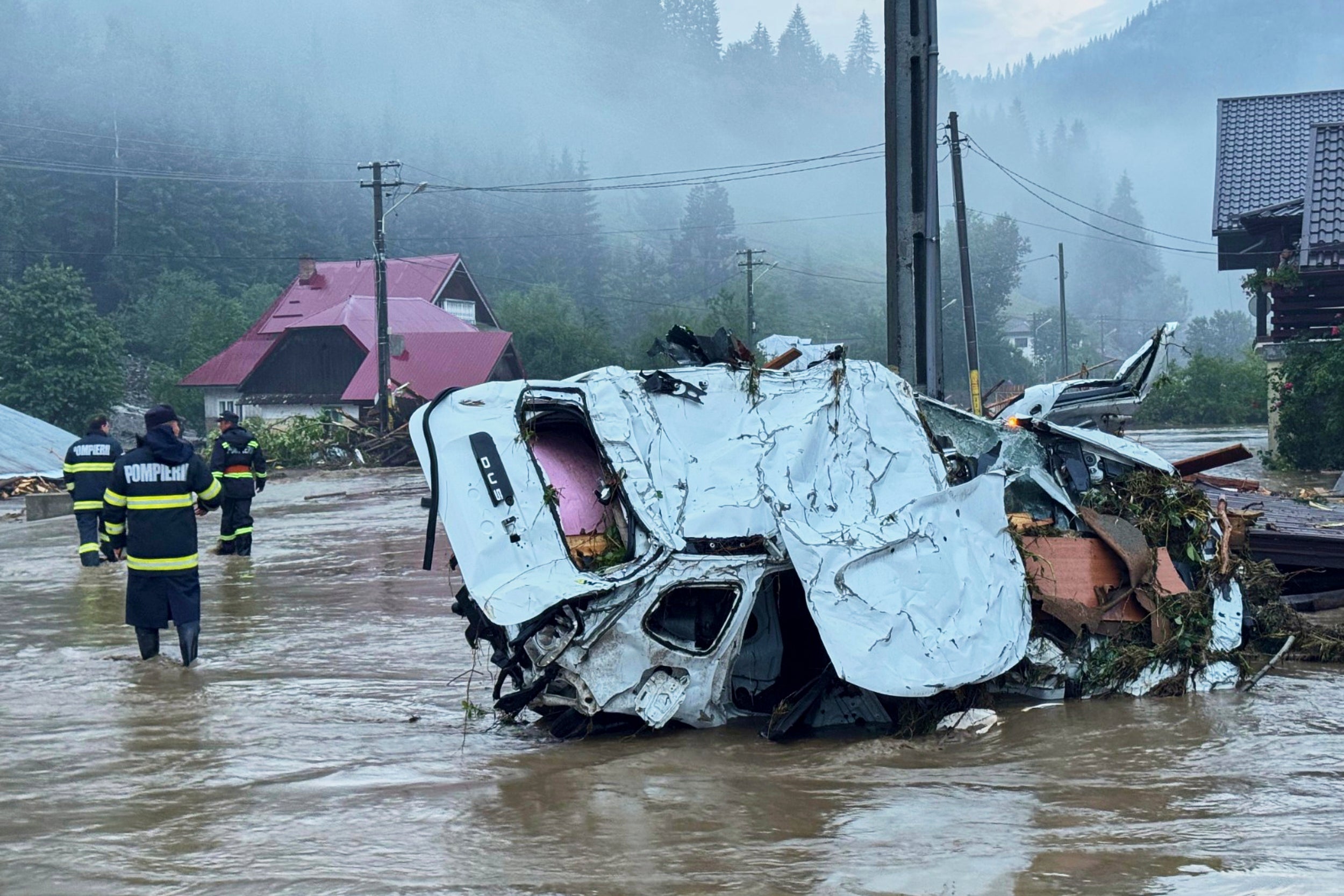 In this image released by the Romanian Emergency Services Suceava (ISU Suceava) first responders walk by damaged vehicles after a flash flood in the village of Brosteni, northern Romania, Monday, July 28, 2025. (Romanian Emergency Services - ISU Suceava via AP)