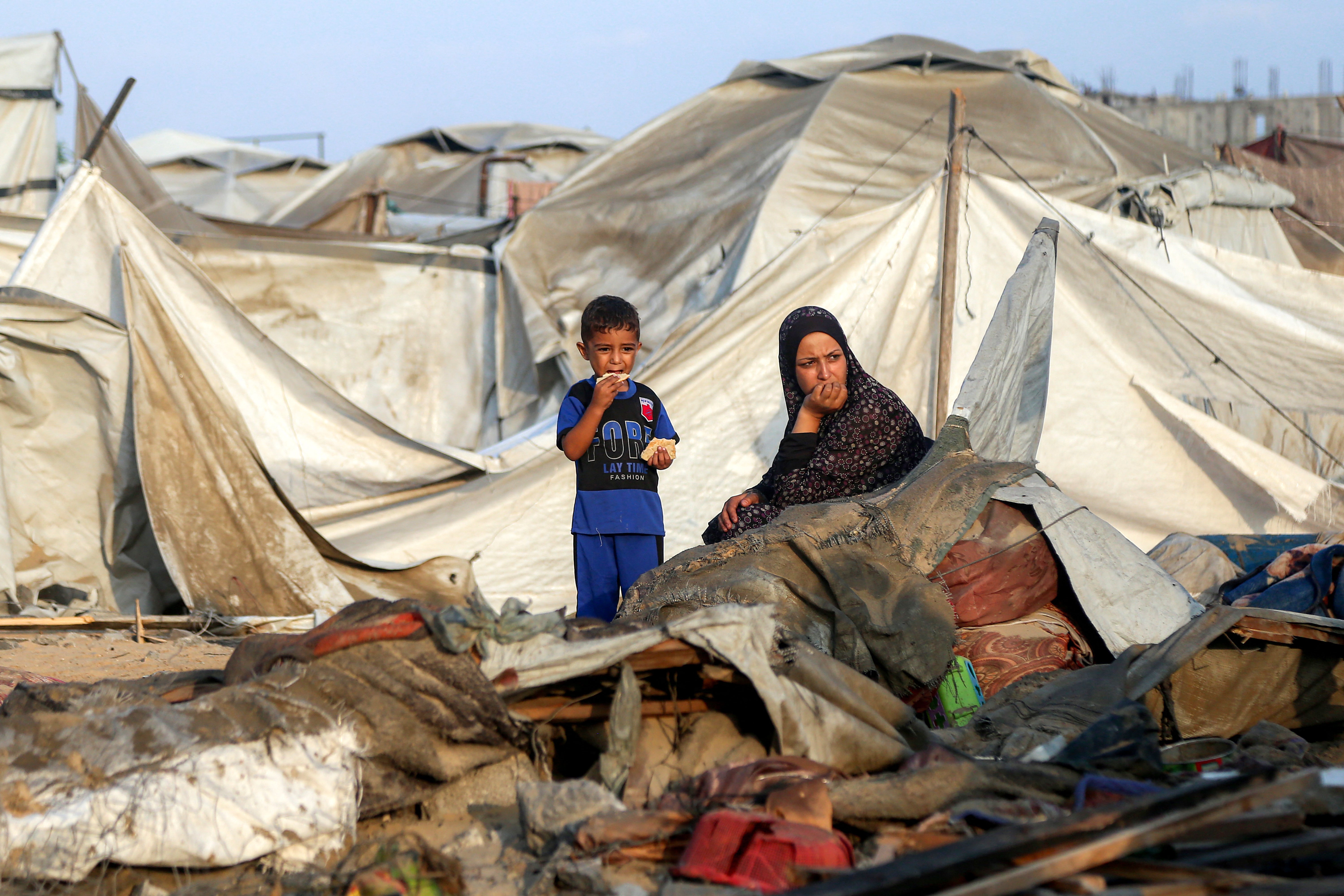 A woman and a boy sit by debris and destroyed tents following overnight Israeli bombardment