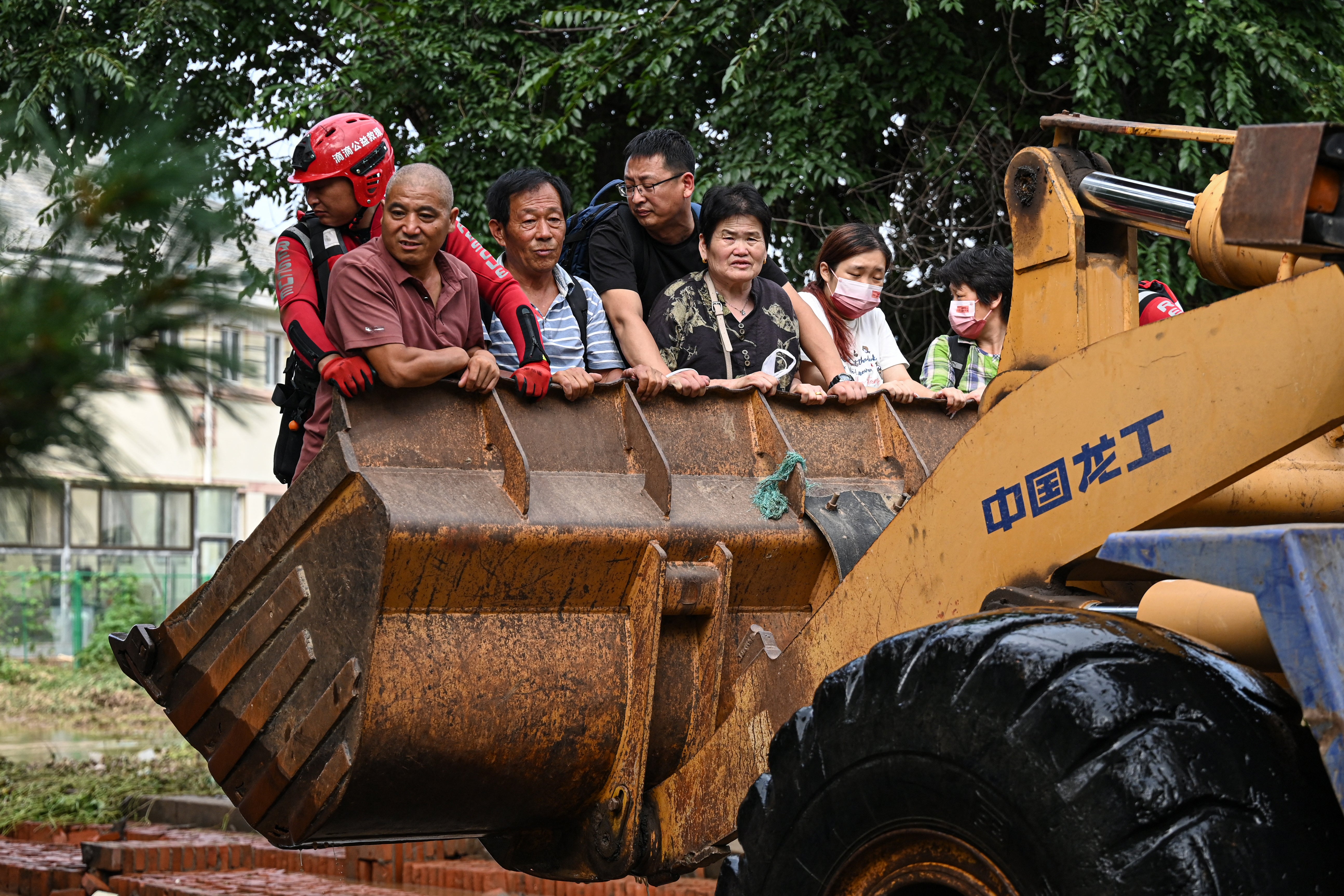 People ride on a front loader to cross a flooded street after heavy rains at Taishitun village in Miyun district on the outskirts of Beijing on 28 July 2025