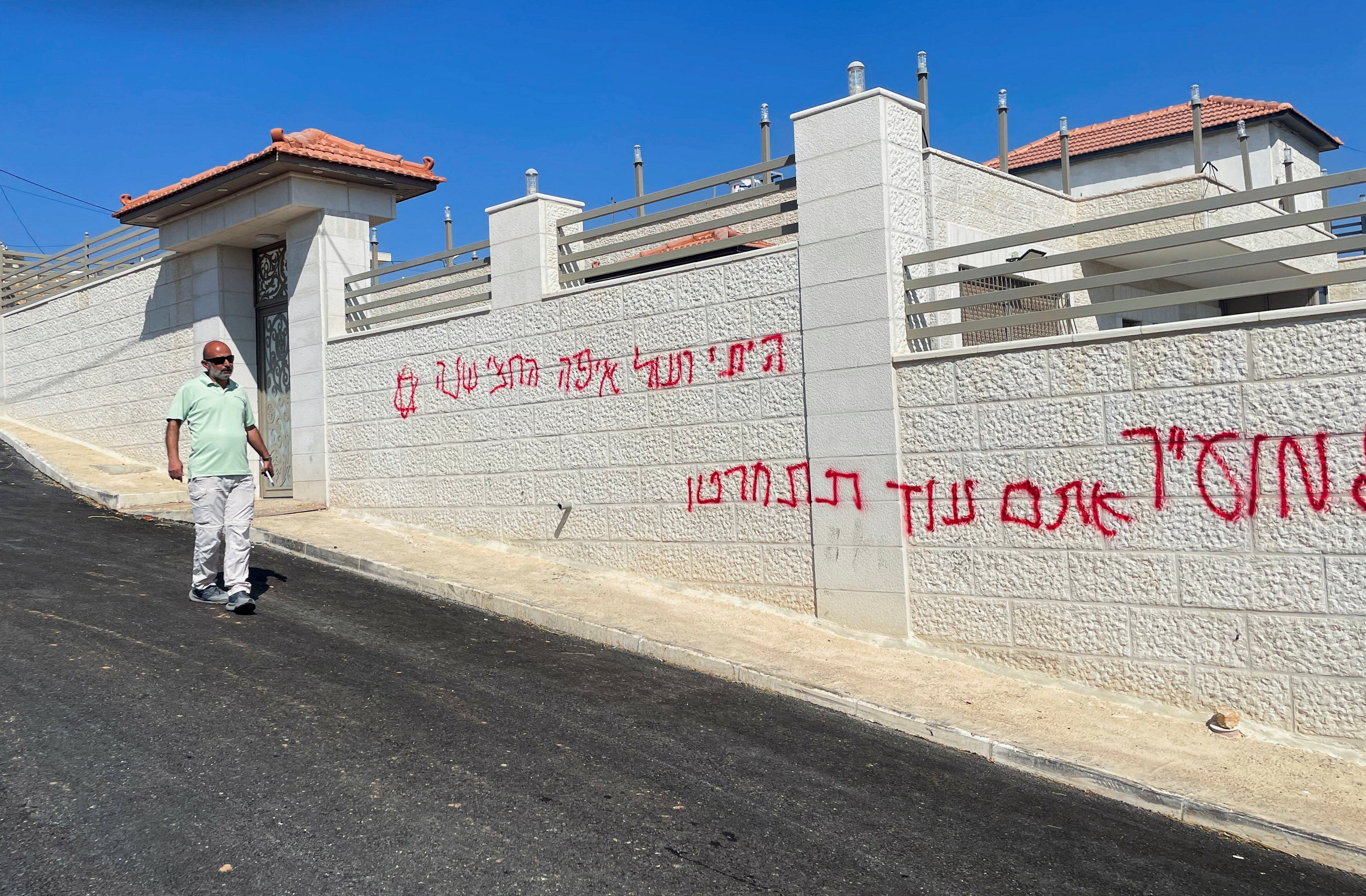 A Palestinian man walks next to a wall covered with sprayed Hebrew slogans following an Israeli settler attack in Taybeh near Ramallah, in occupied West Bank, on 28 July 2025