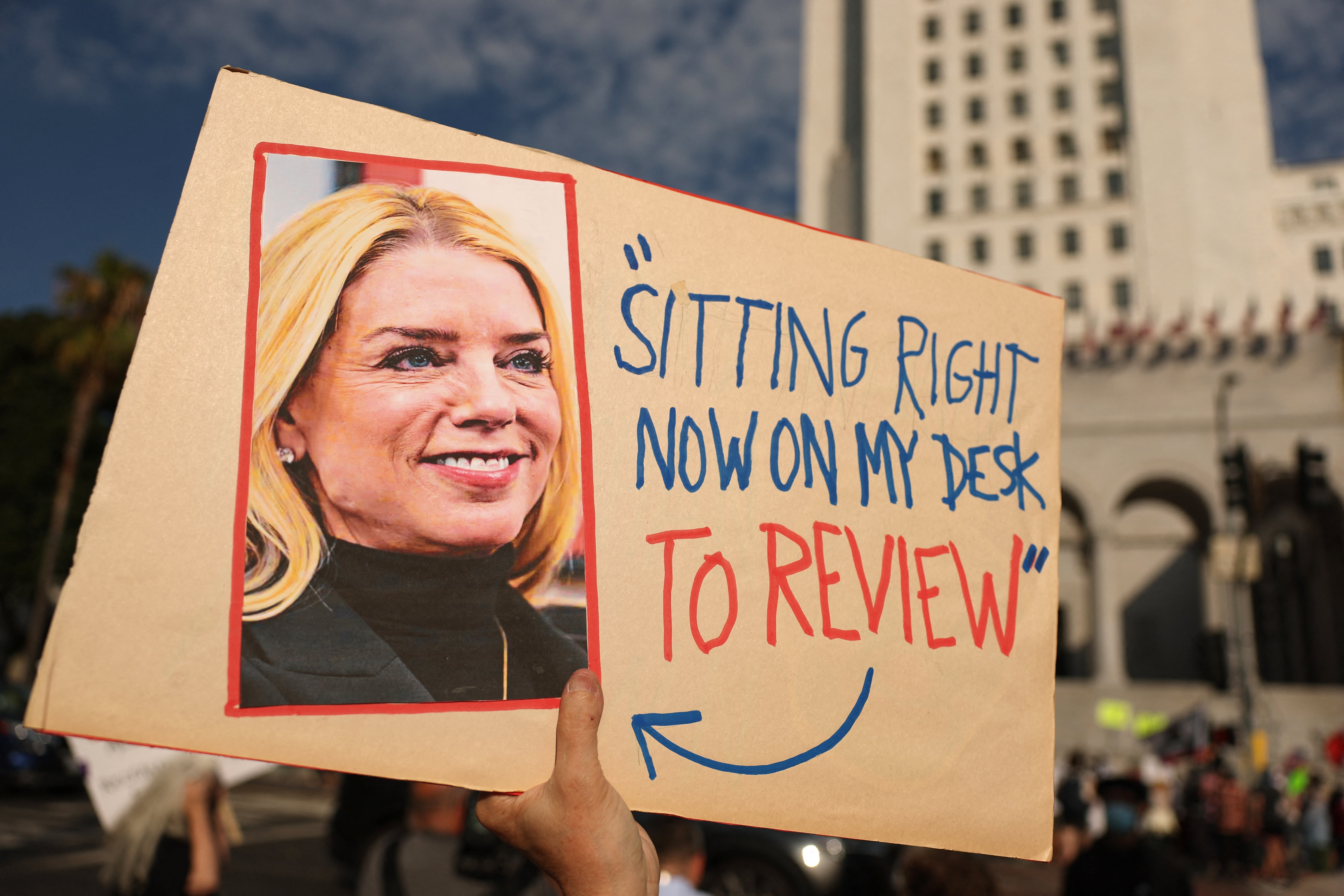 A person holds a sign with a photo of Attorney General Pam Bondi and her quote claiming the 'client list' was sitting on her desk during a protest in Los Angeles