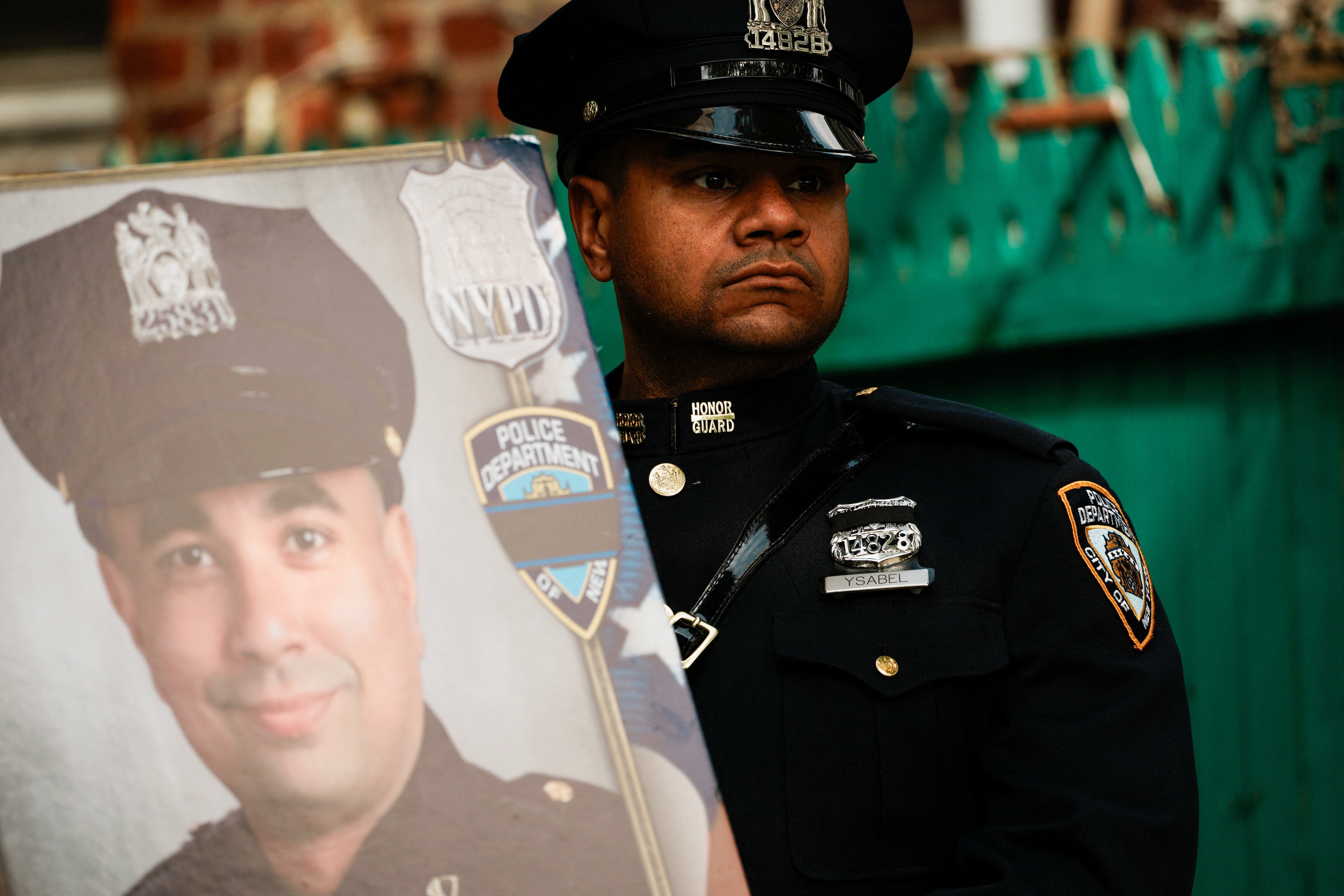A police officer stands next to a picture of NYPD officer Didarul Islam, killed in the Midtown mass shooting