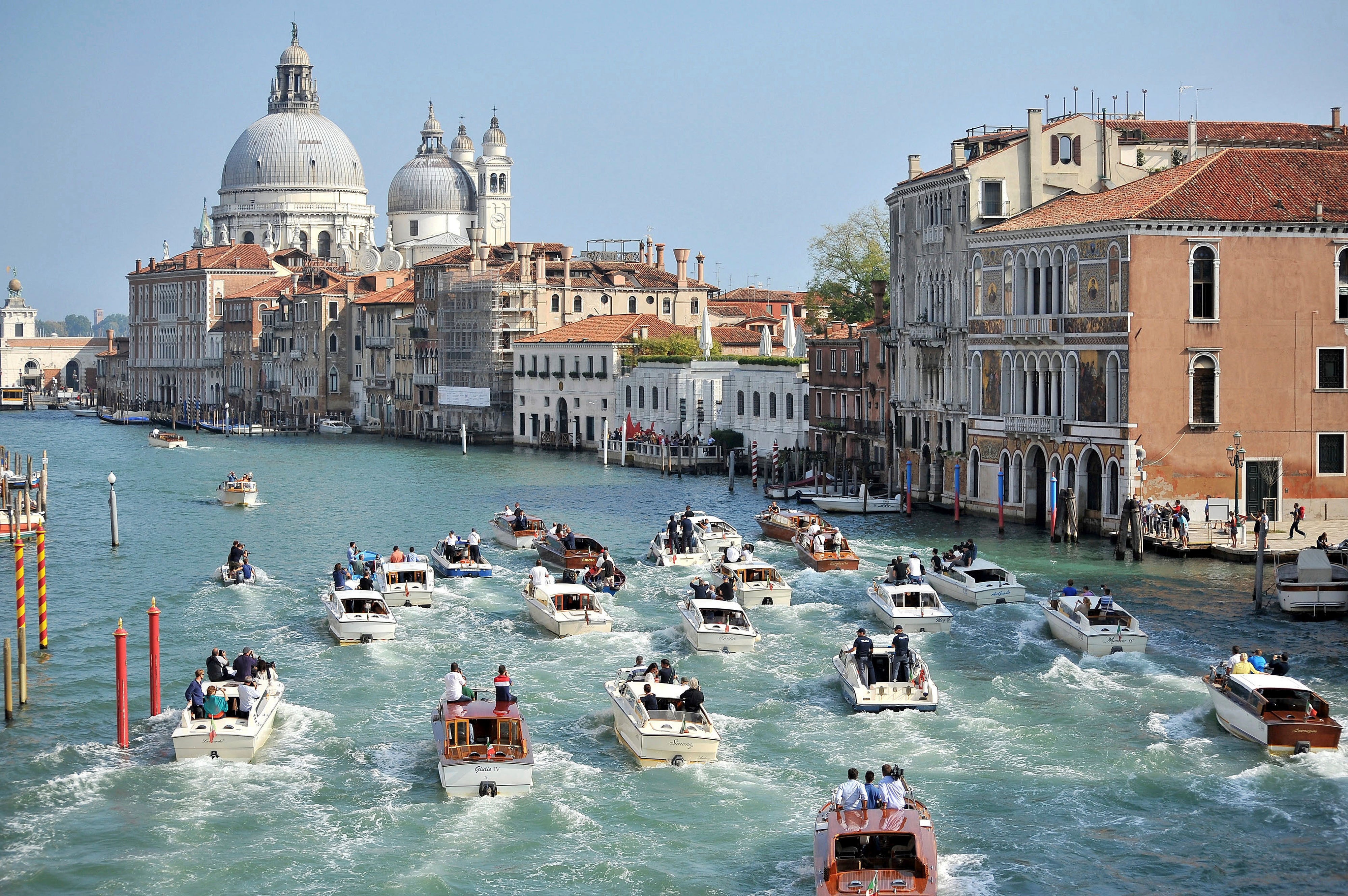 The boat carrying George Clooney and his wife, Amal Alamuddin, is surrounded by media and security boats as they cruise the Grand Canal after leaving the Aman luxury Hotel in Venice, Italy, Sept. 28, 2014. (AP Photo/Luigi Costantini, File)