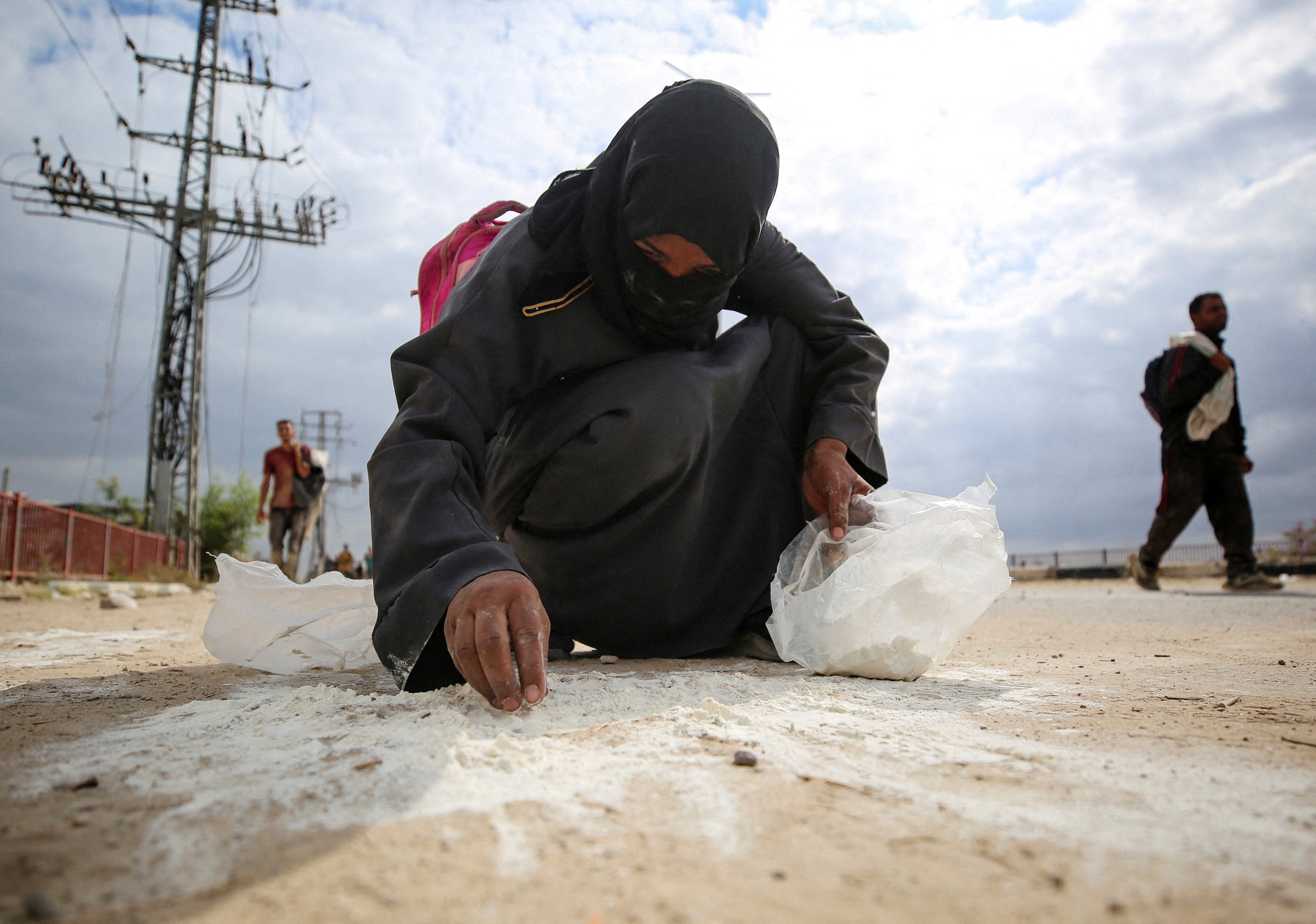 A woman collects flour from the ground as Palestinians receive aid supplies from the US-backed Gaza Humanitarian Foundation