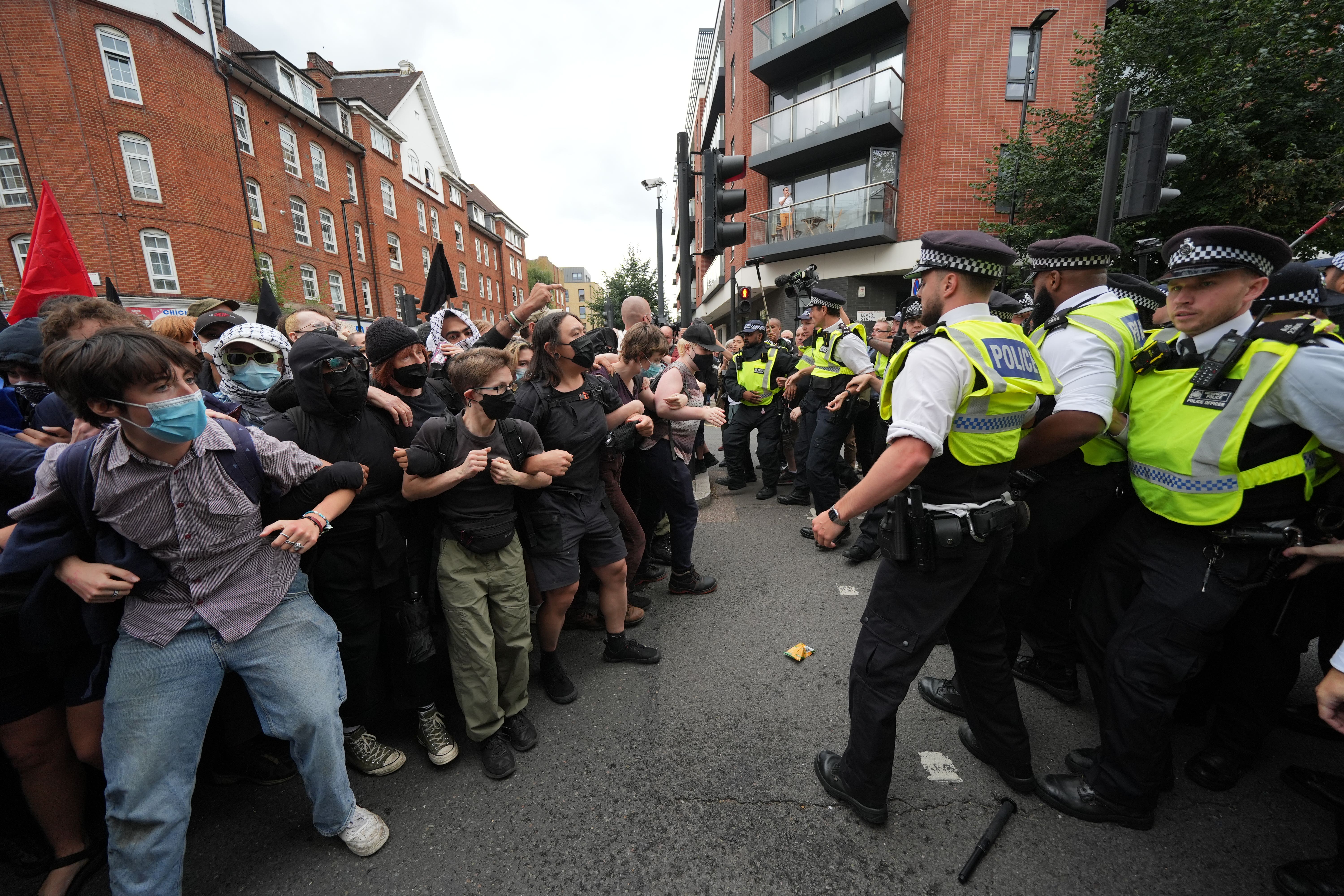 Police form a barrier in front of masked protesters outside the central London hotel