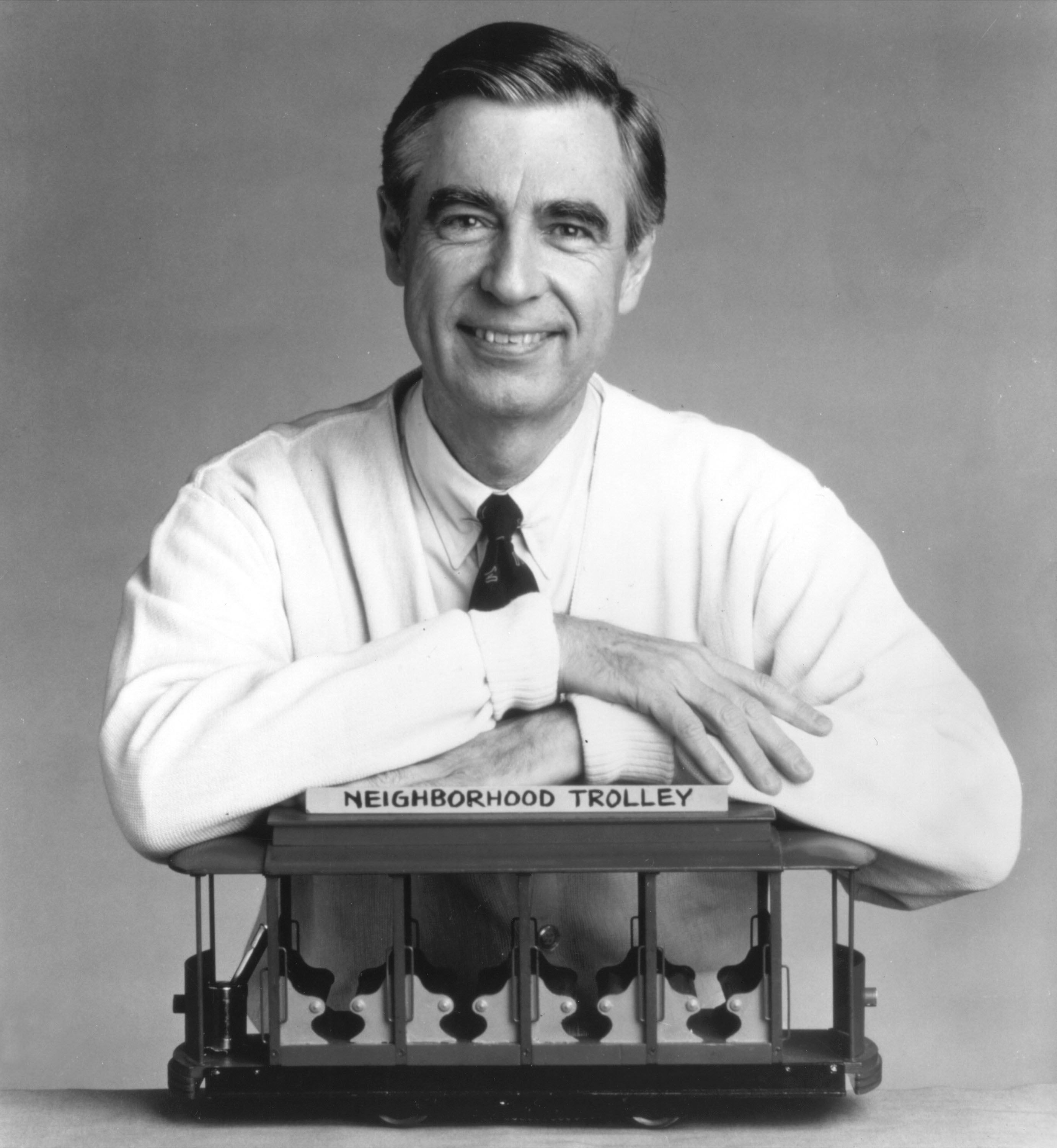 Fred Rogers rests his arms on a small trolley in this promotional portrait. He mainly taught children social skills in his program