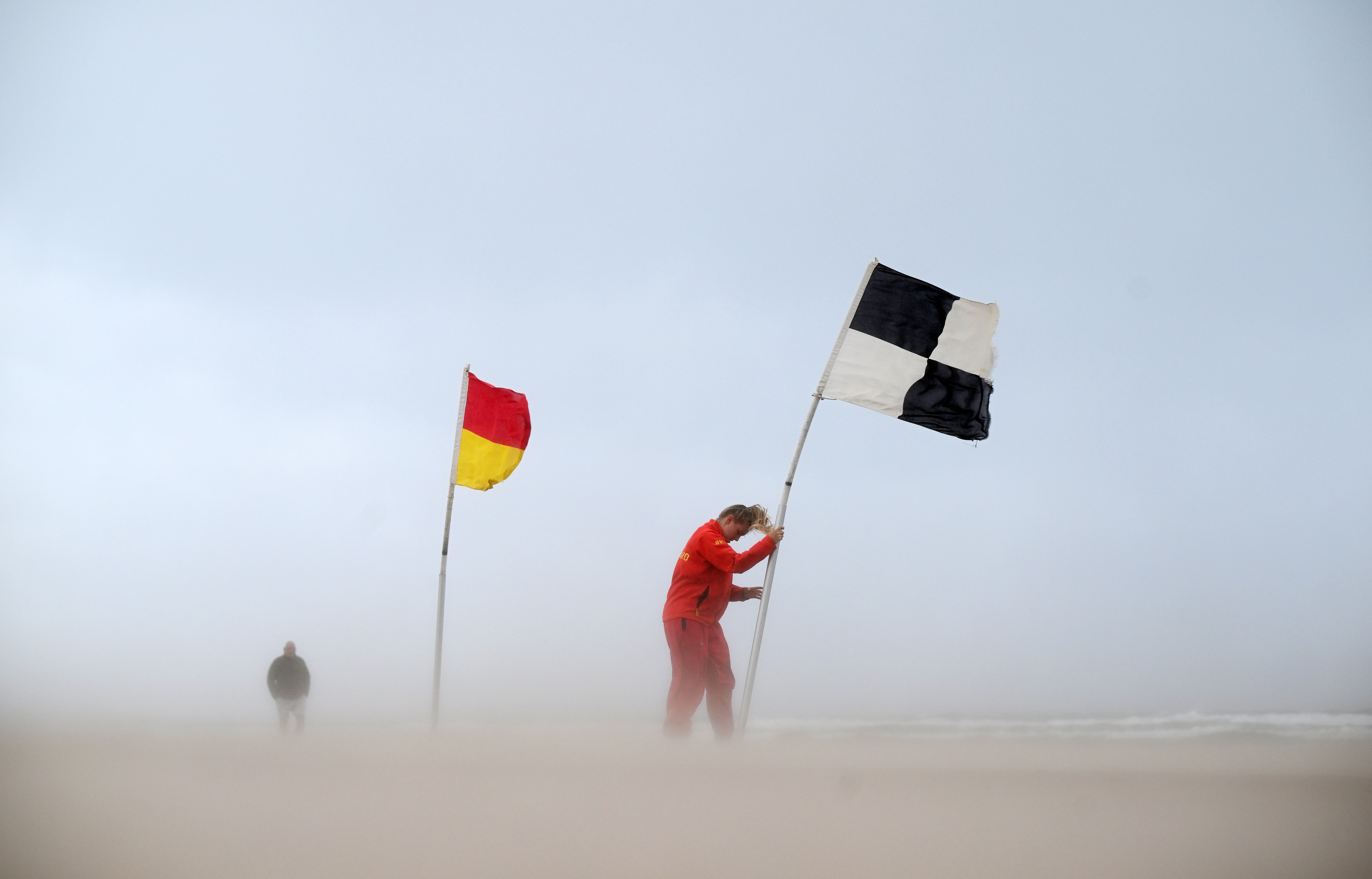 <p>An RNLI lifeguard battles with a flag amid winds in Northern Ireland</p>