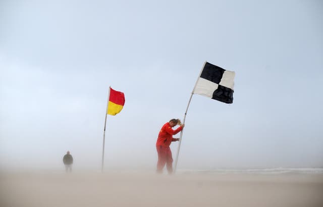 <p>An RNLI lifeguard battles with a flag amid winds in Northern Ireland</p>
