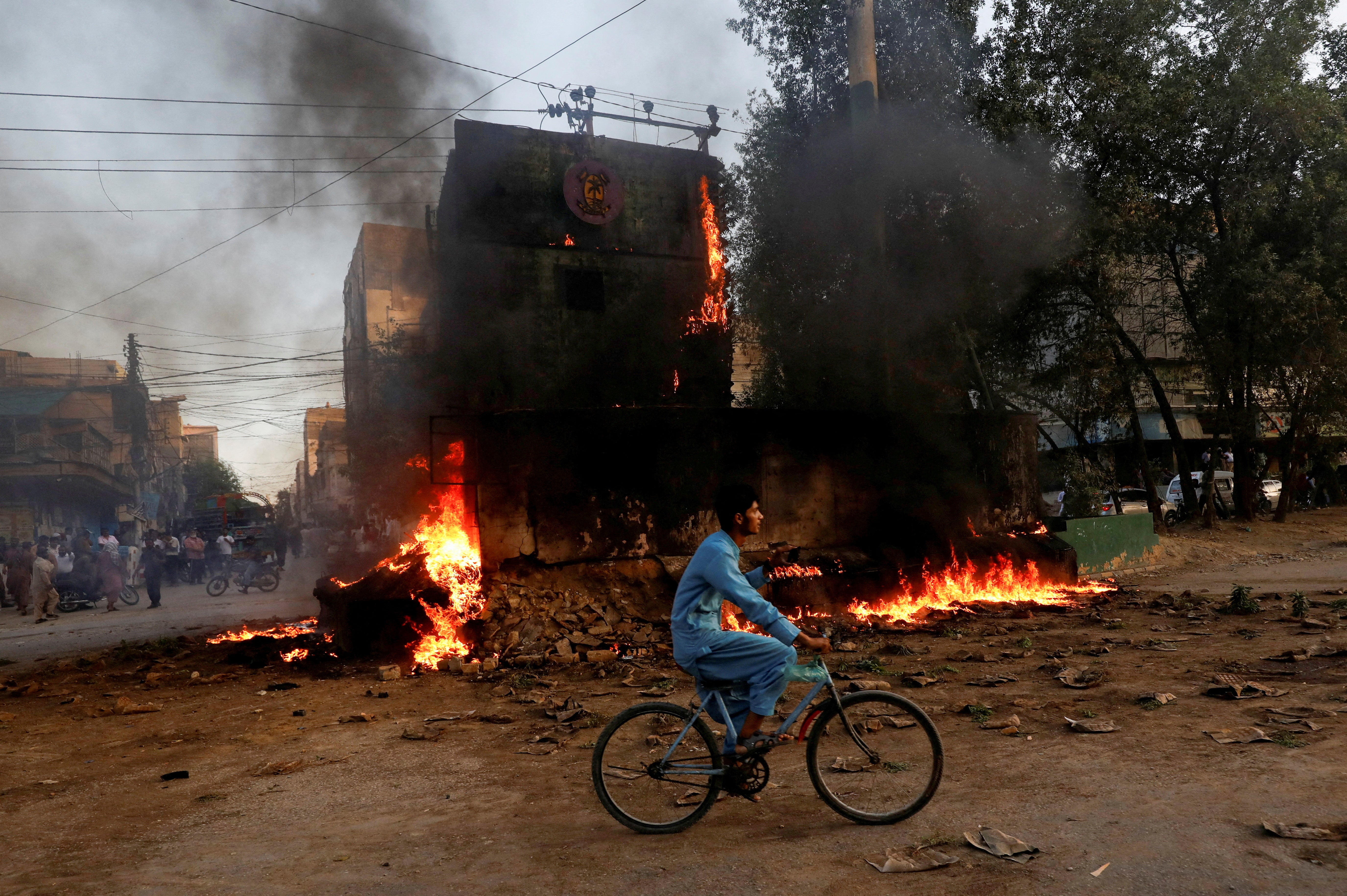 File. A boy rides past a paramilitary checkpoint set on fire by supporters of former prime minister Imran Khan during a protest against his arrest in Karachi, Pakistan, on 9 May 2023