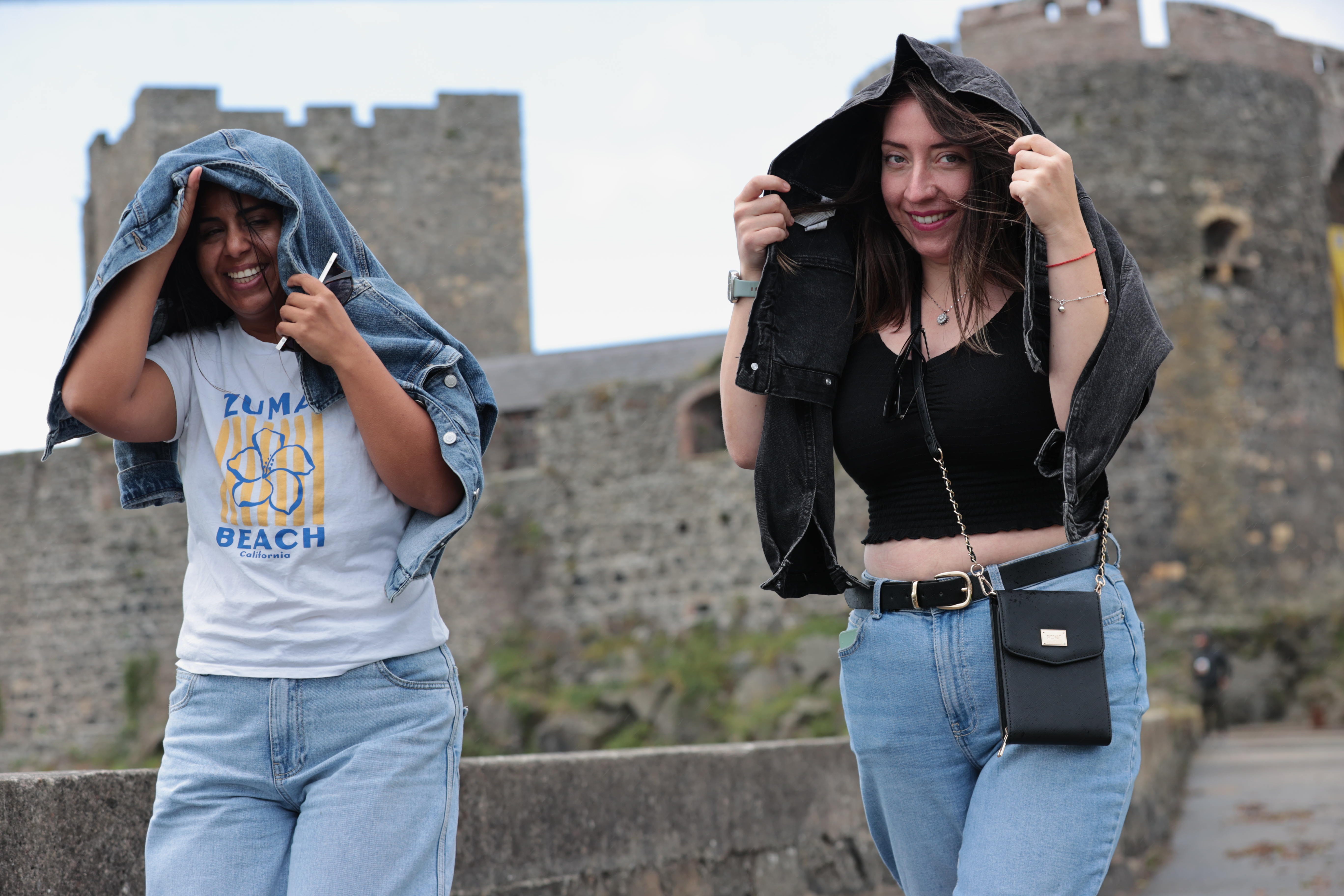 Giselle Munoz Alarcon (left) and Dominica Sepulveda Gutierrez shield from the wind at Carrickfergus Castle, Co Antrim (Liam McBurney/PA)