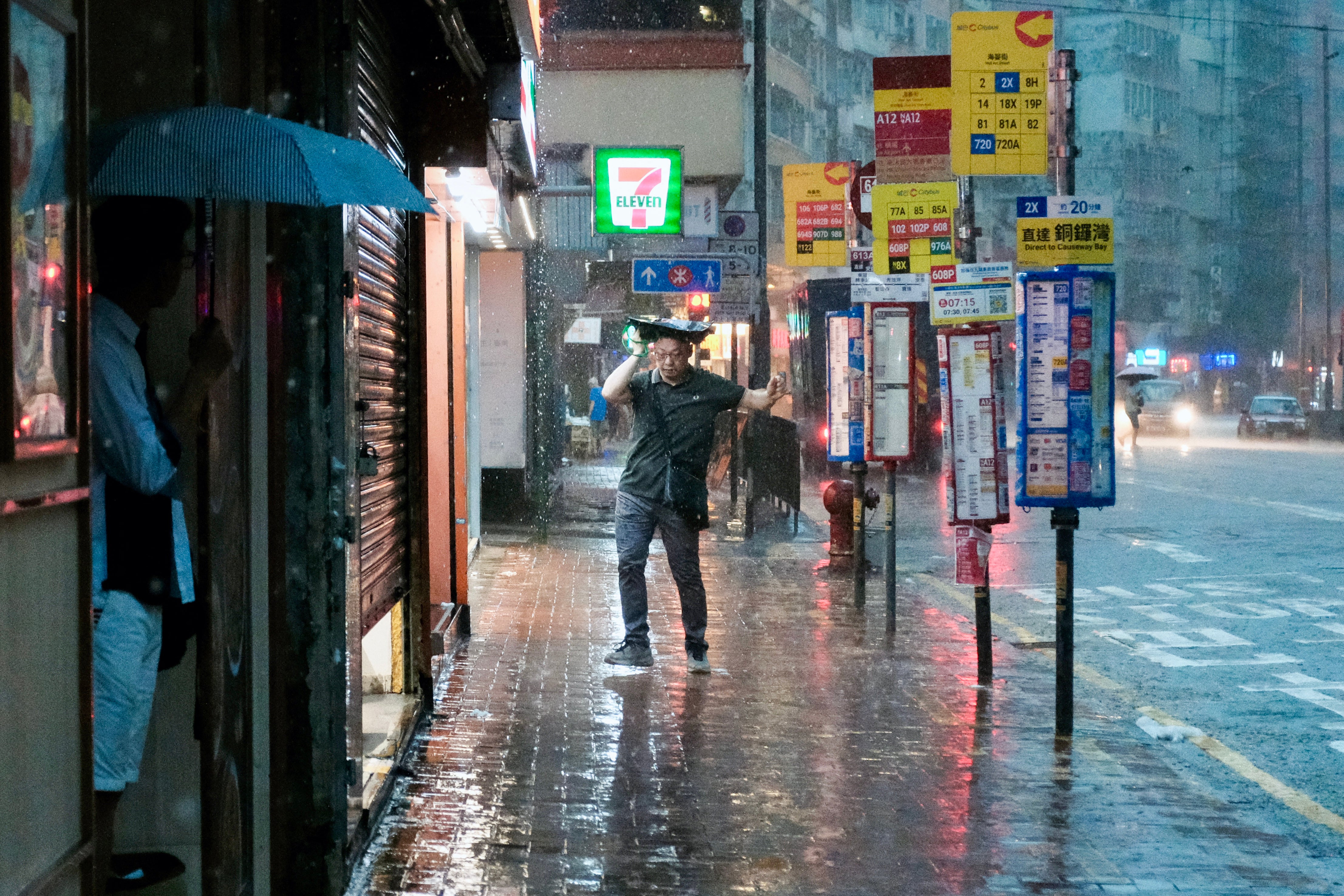 A pedestrian holds a bag over his head beside a bus stop in the Quarry Bay area of Hong Kong on 5 August 2025