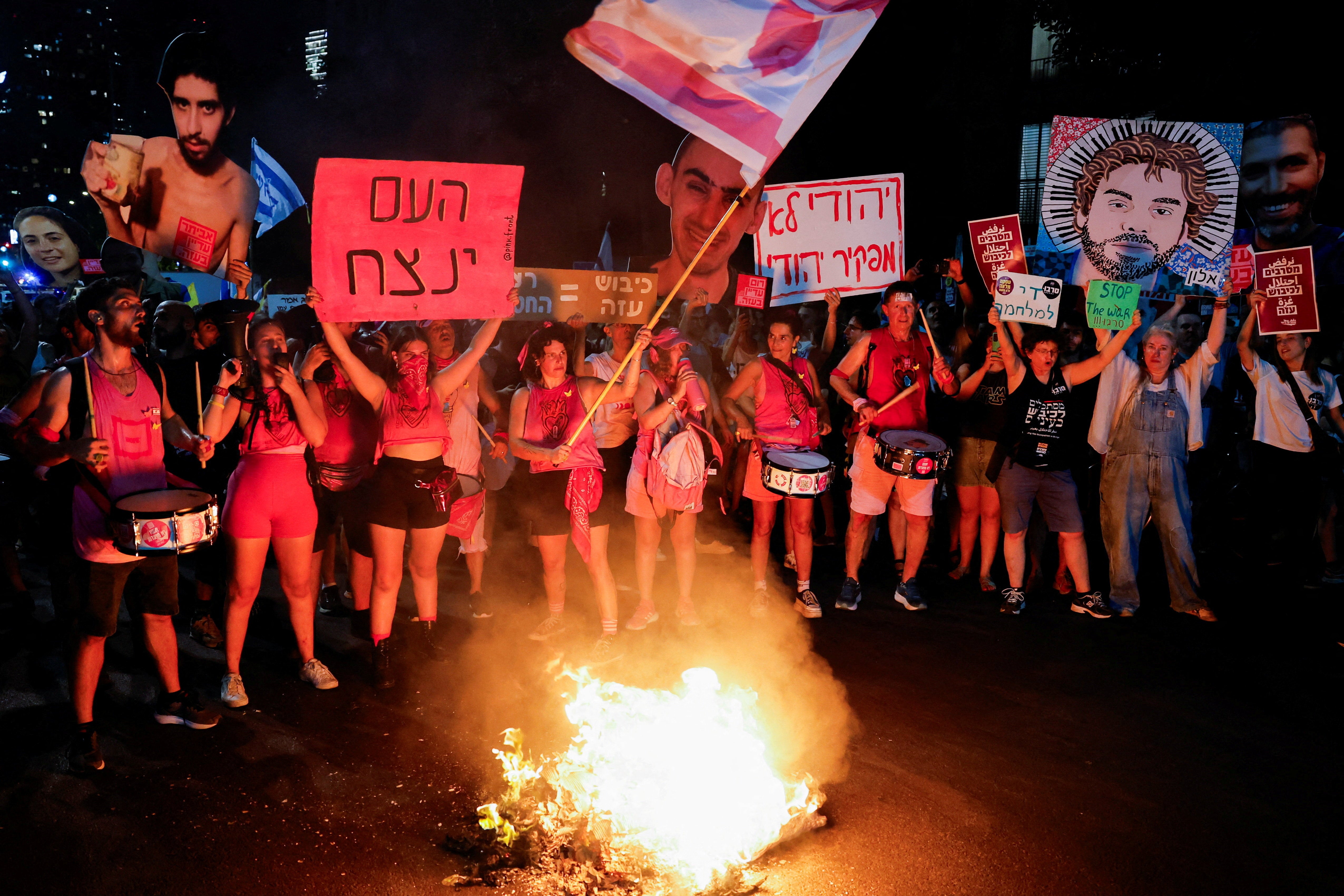 Demonstrators and relatives of hostages kidnapped during the deadly October 7, 2023, attack on Israel by Hamas, protest demanding the immediate release of the hostages and the end of the war, as a fire burns in Tel Aviv, Israel, August 7, 2025