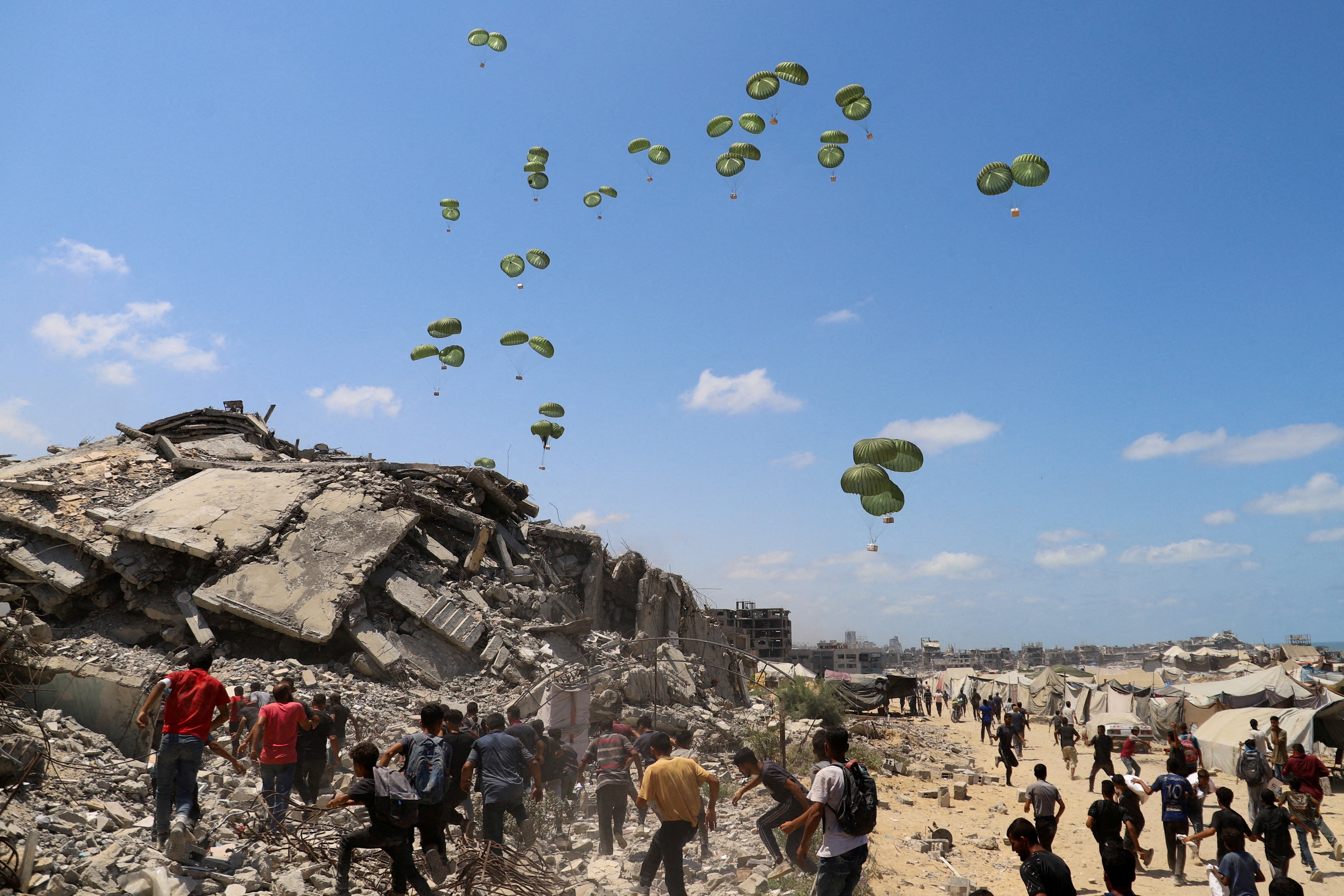 Palestinians run towards parachutes carrying aid packages airdropped over northern Gaza Strip