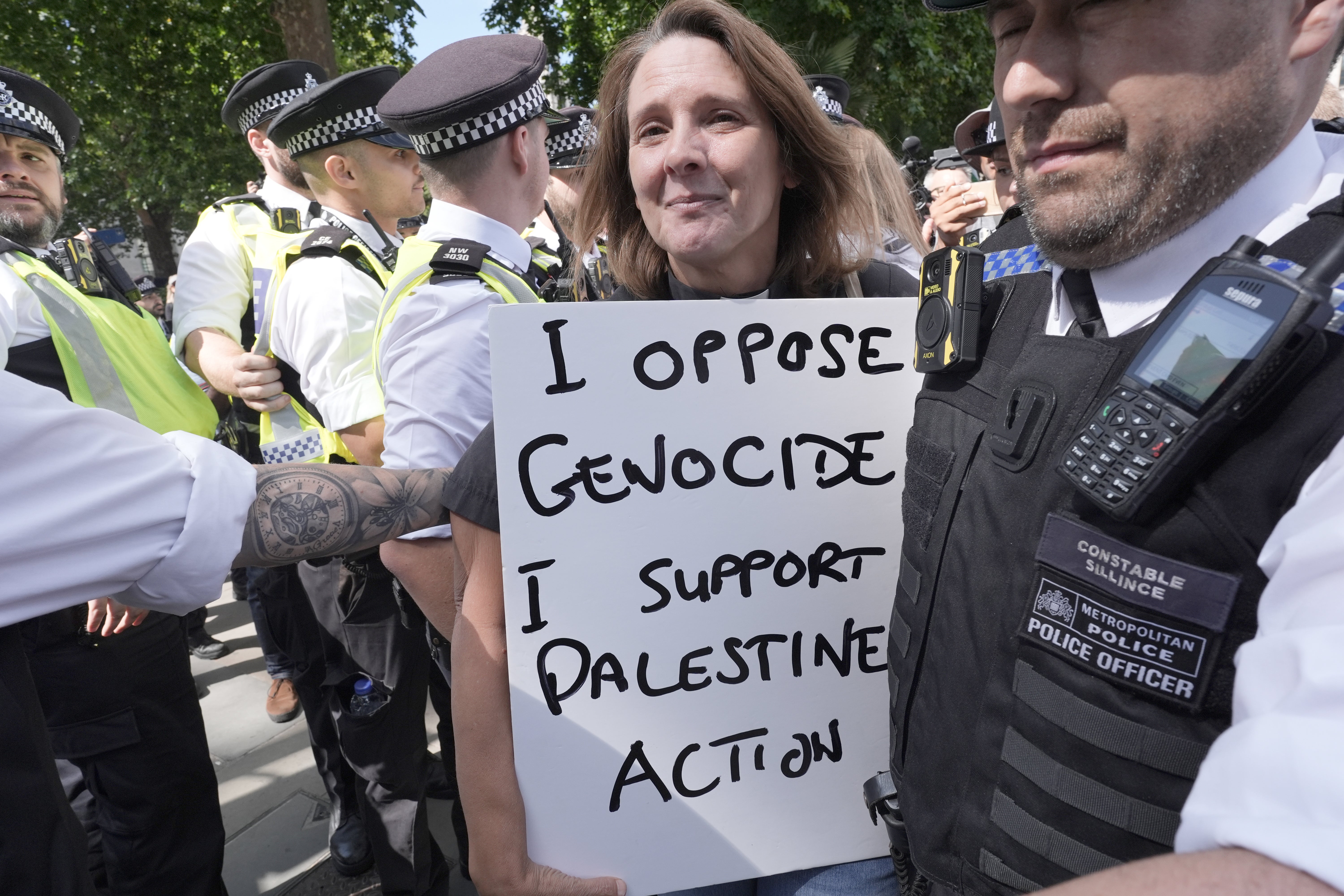 A woman holding a placard at the rally for Palestine Action is led away by police officers