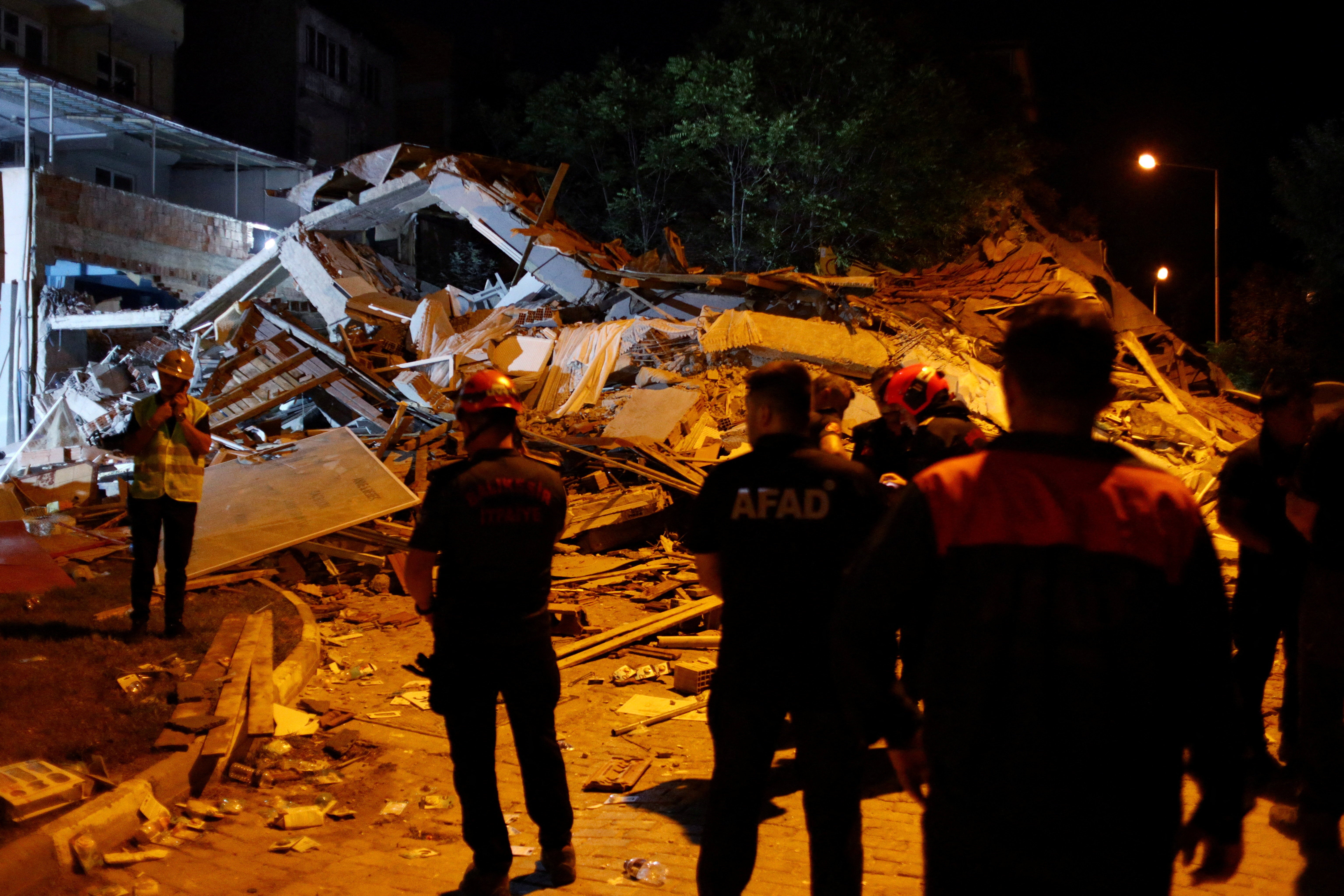 Turkish search and rescue personnel stand next to a collapsed building after an earthquake in Sindirgi