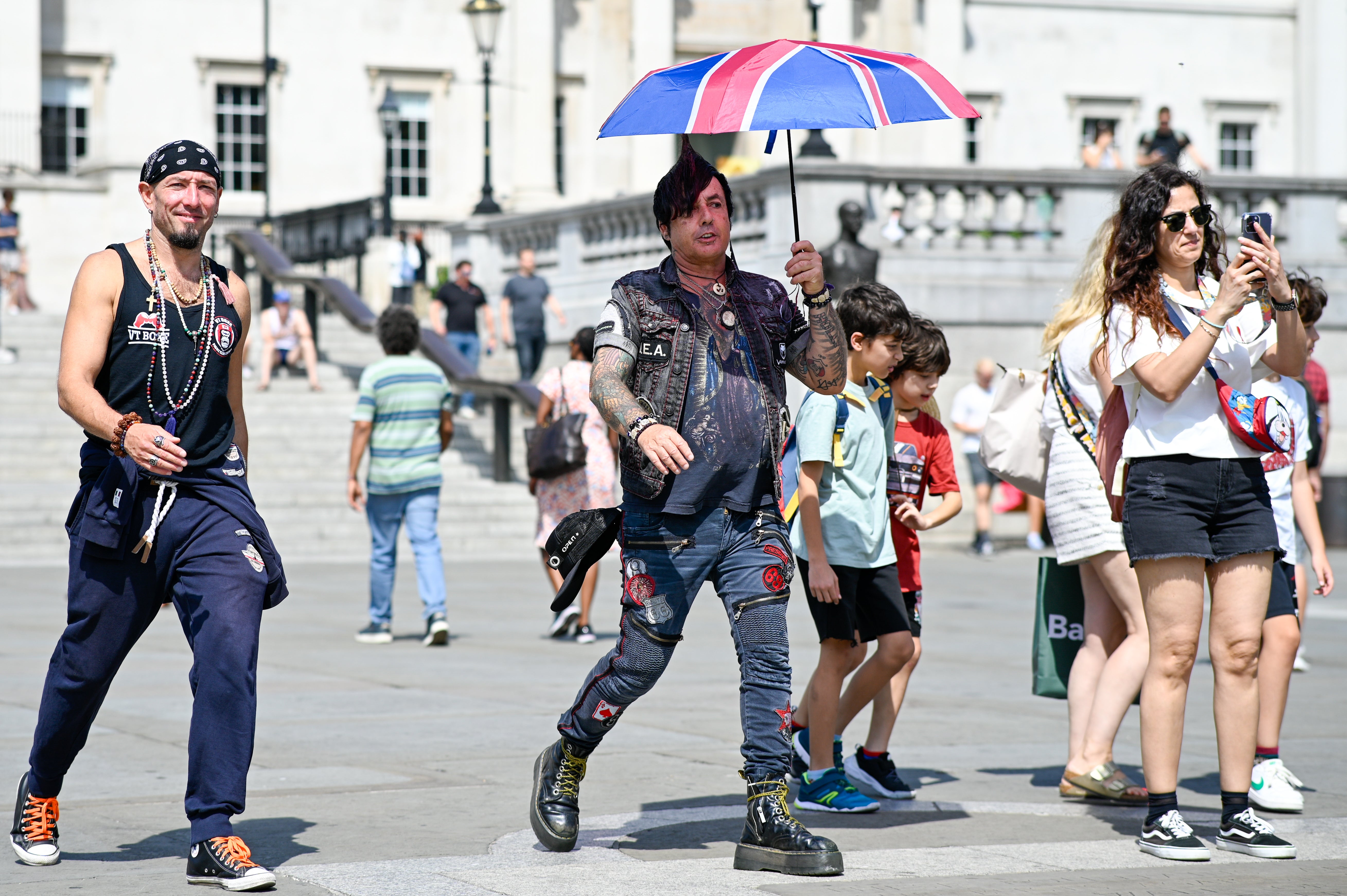 Members of the public with a Union Jack umbrella walk through Trafalgar Square during a heatwave on August 12, 2025 in London