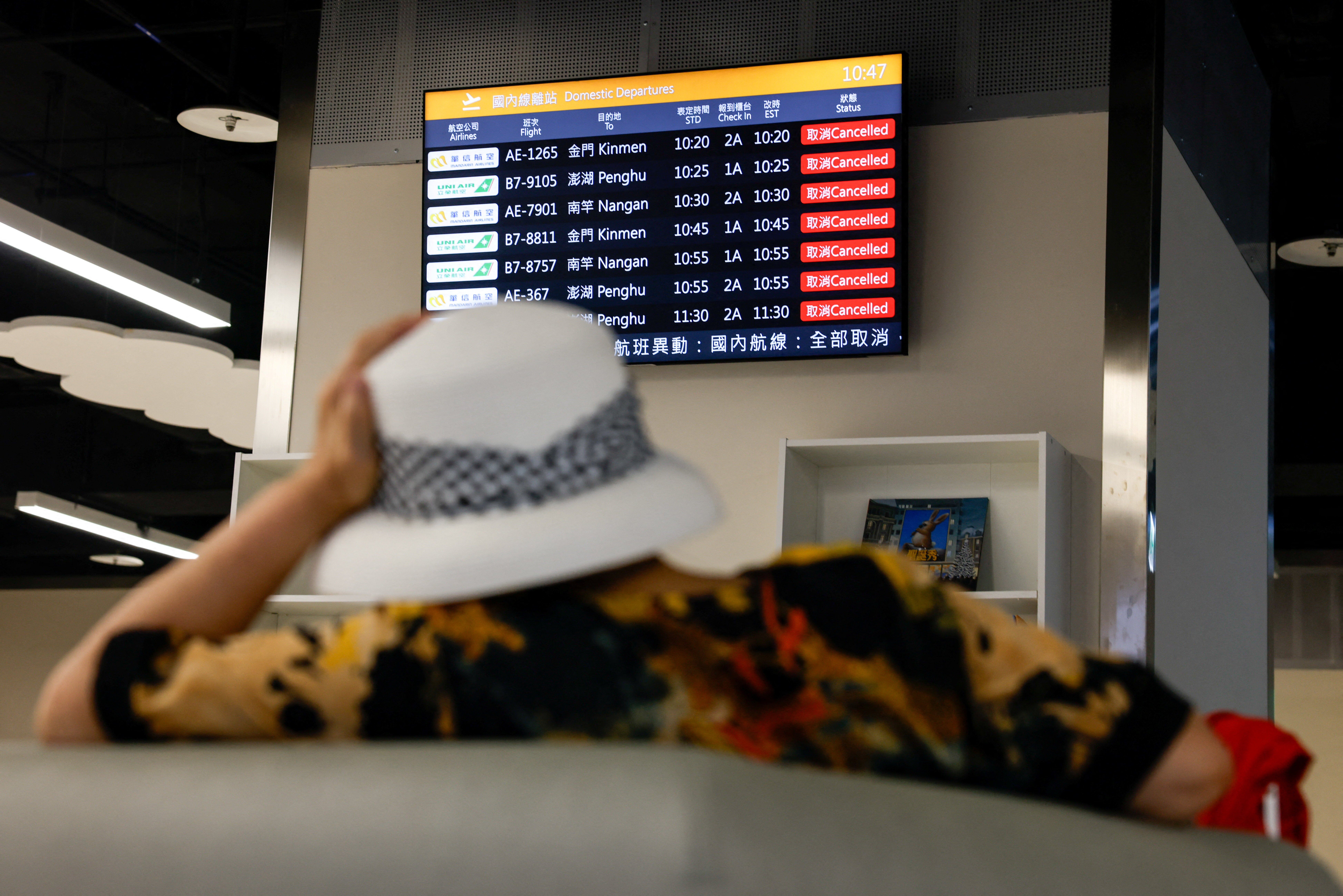 A woman sits in front of a screen displaying information on cancelled domestic flights, as Typhoon Podul approaches the country, in Taipei, Taiwan