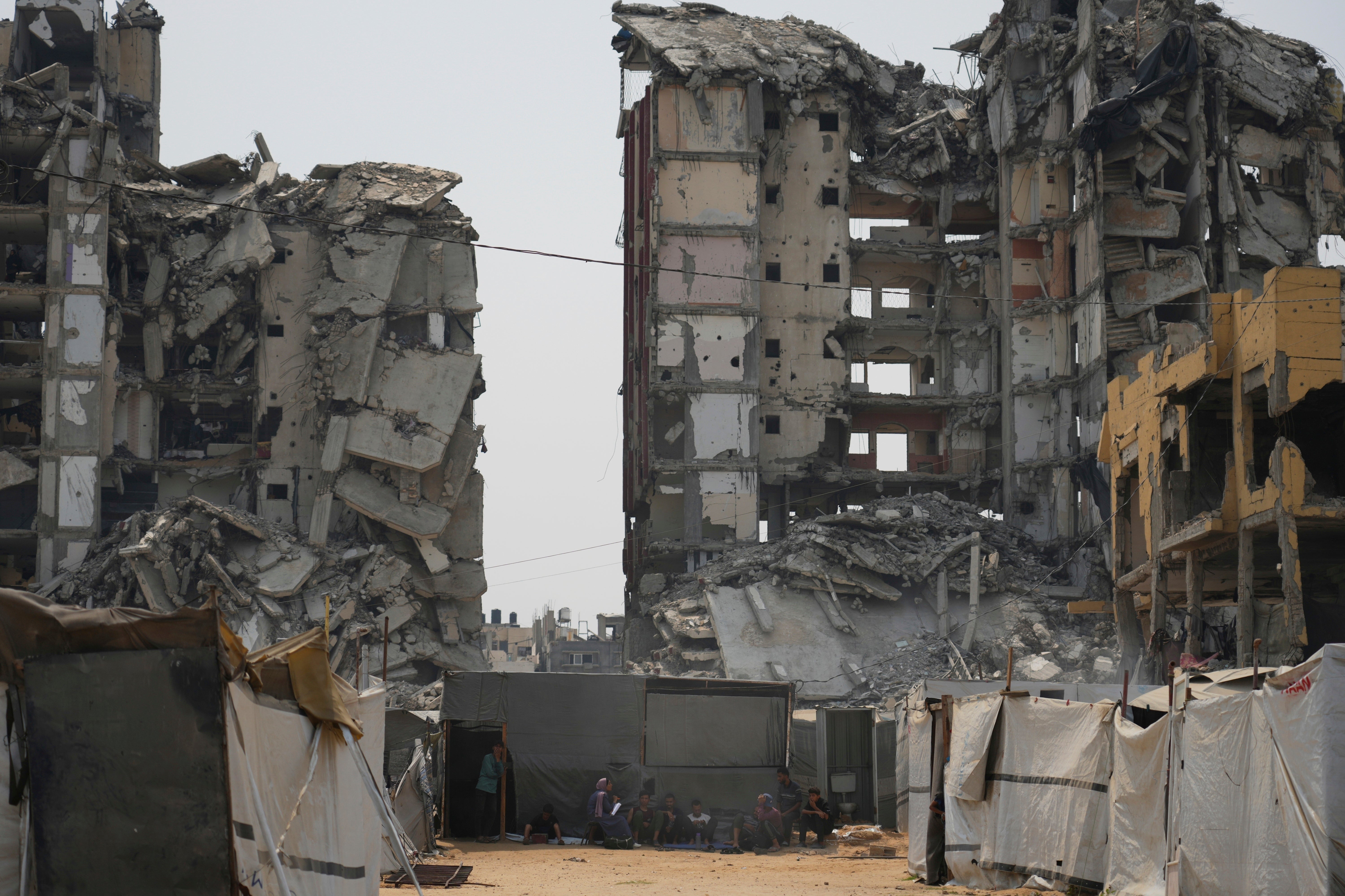 A group of Palestinians sit in the shade of their tent amid destroyed buildings on a hot summer day in Gaza City, 12 August 2025