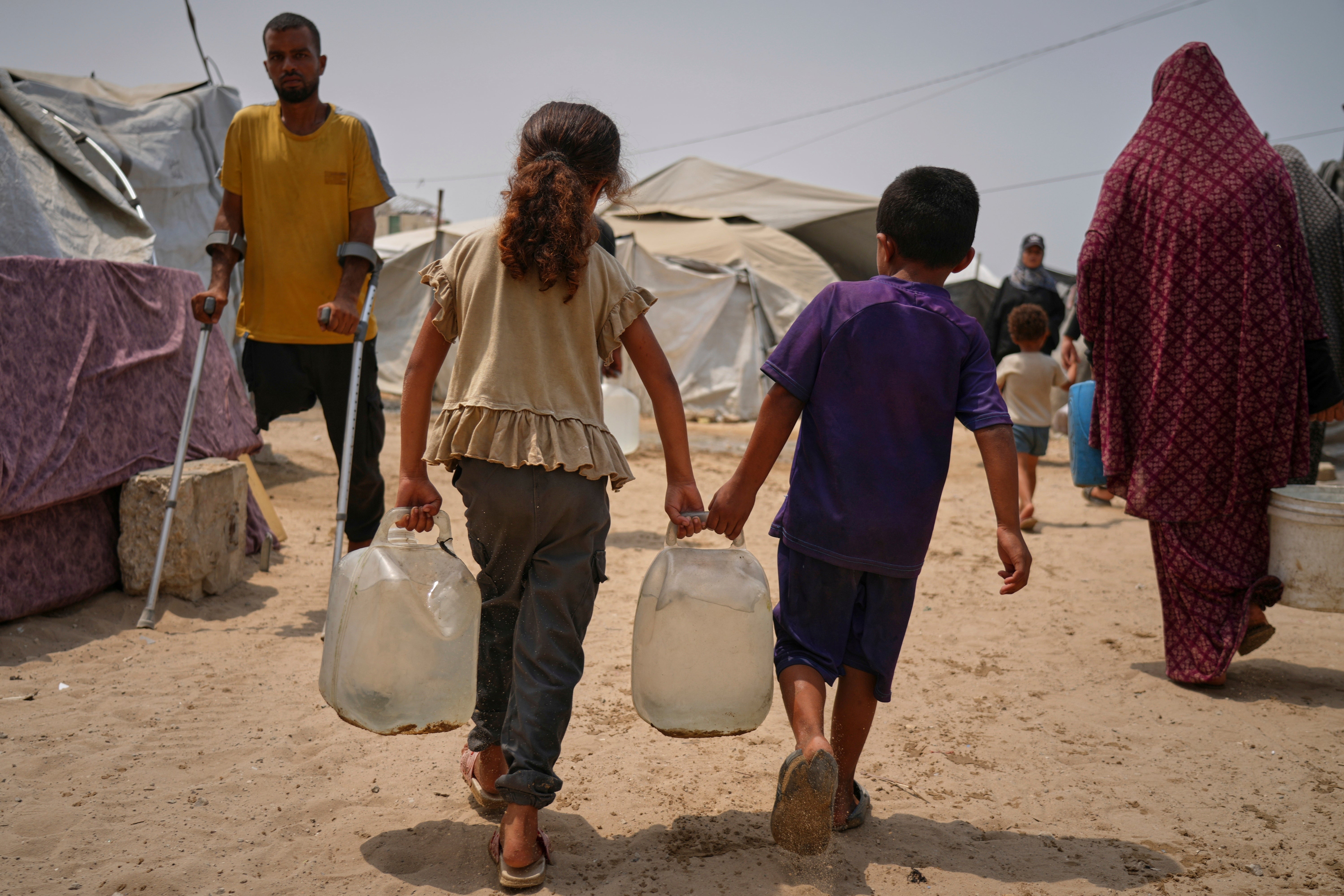 In the summer heat, Palestinian children carry jerrycans after collecting water from a distribution point in Gaza City, 12 August 2025