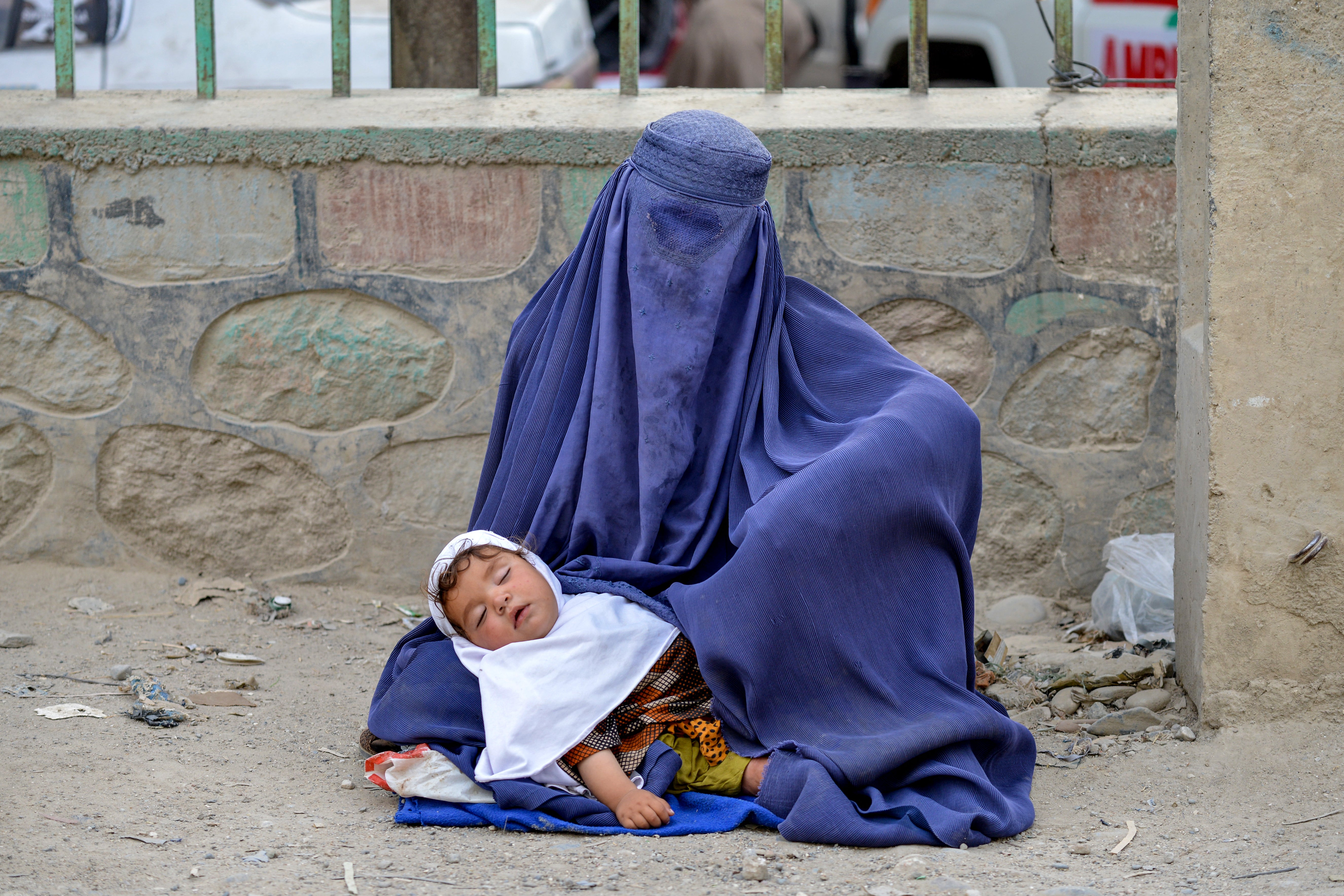 An Afghan burqa-clad woman carrying a child seeks alms along a road in the Argo district of Badakhshan province