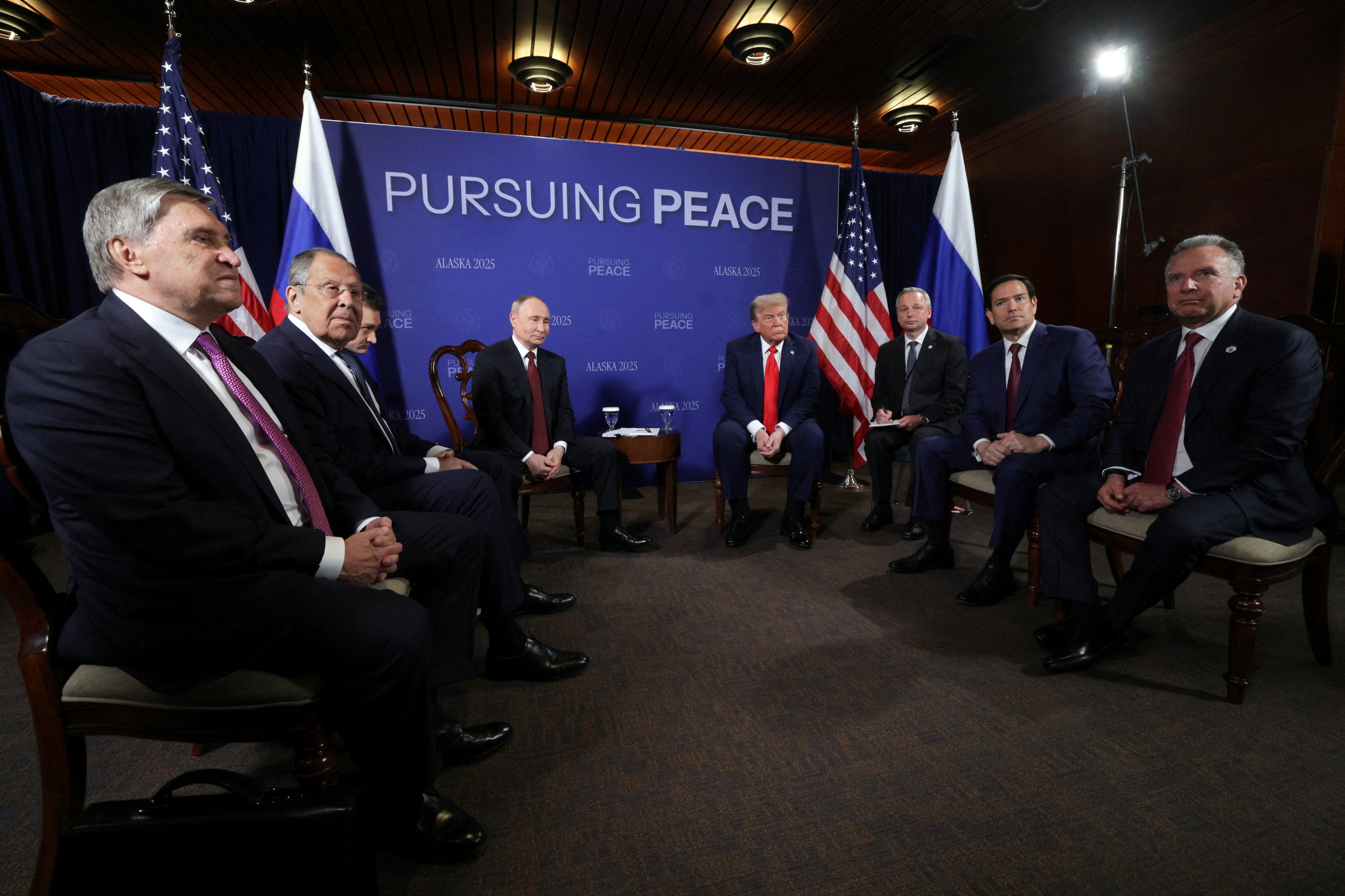 Russian President Vladimir Putin and U.S. President Donald Trump attend a meeting, as Russian Presidential Aide Yury Ushakov, Russian Foreign Minister Sergey Lavrov, U.S. Secretary of State Marco Rubio and U.S. Special Envoy Steve Witkoff sit nearby, at Joint Base Elmendorf-Richardson in Anchorage, Alaska